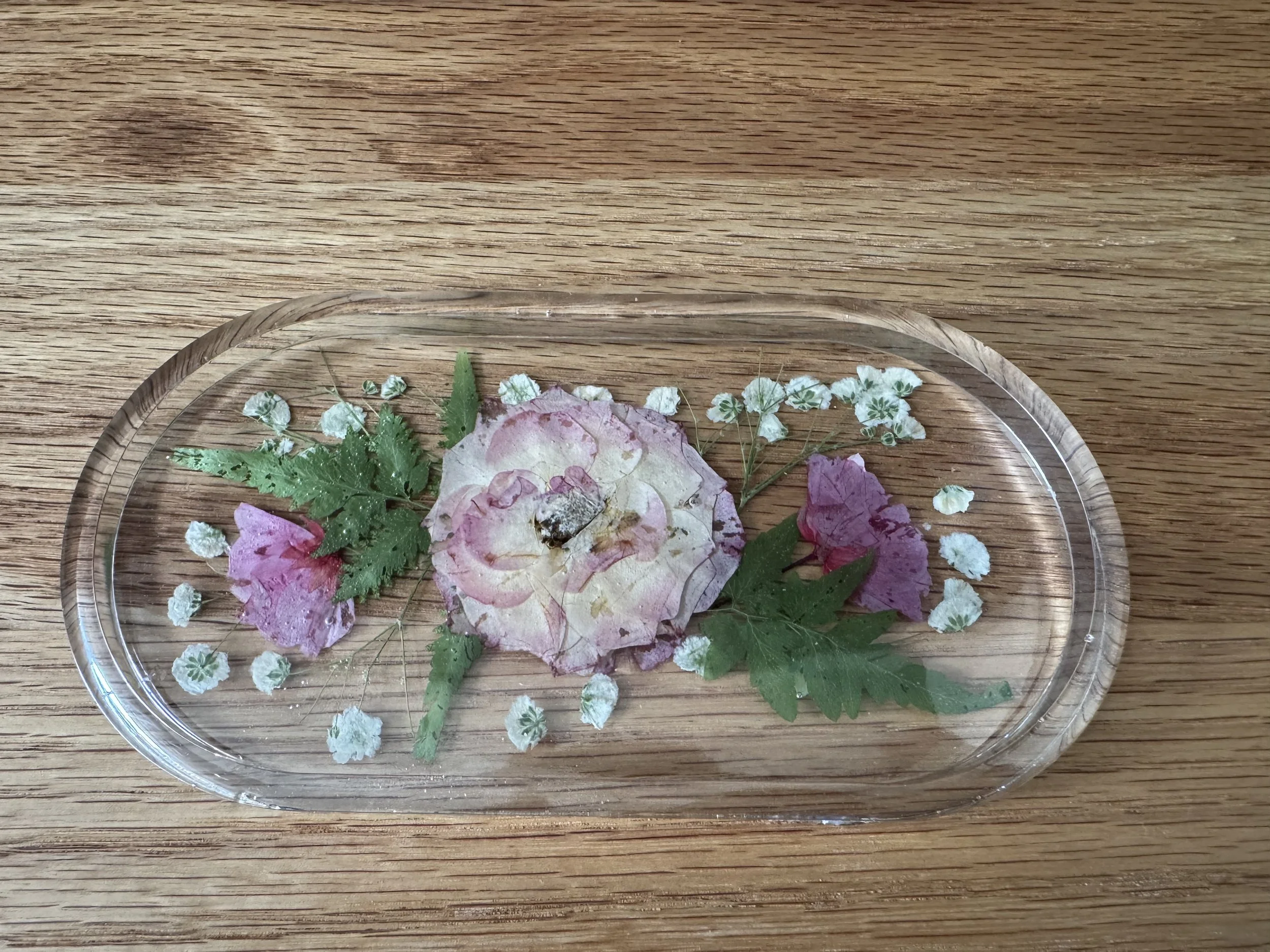 A glass plate with dried flower petals and small white dried flowers on a wooden surface.