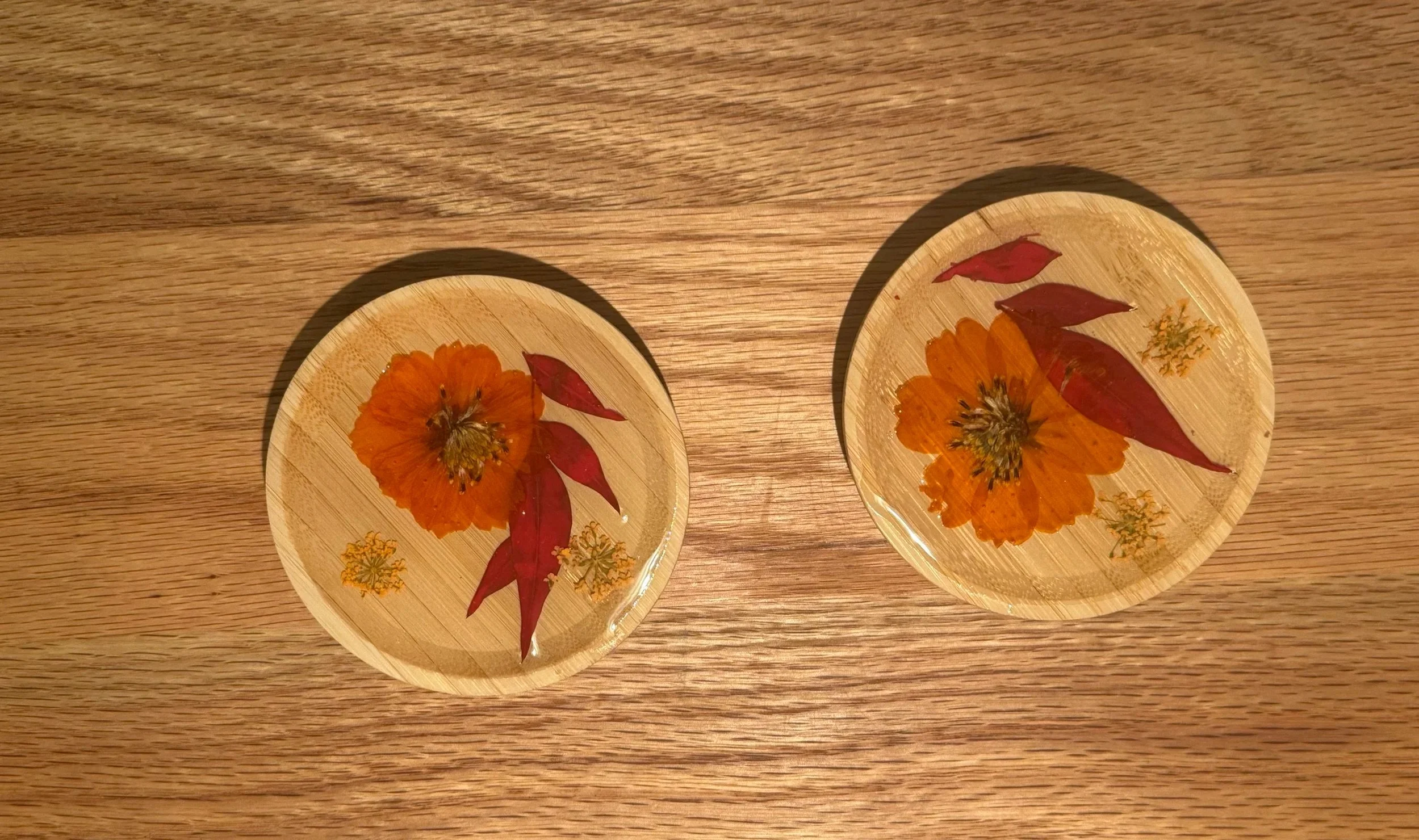 Two glass bowls with preserved orange flowers and red and yellow leaves on a wooden surface.