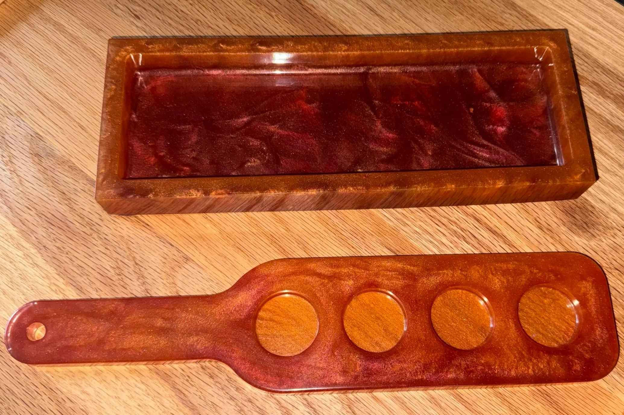A wooden tray of round makeup or eyeshadow pans and a small wooden palette on a wooden table.