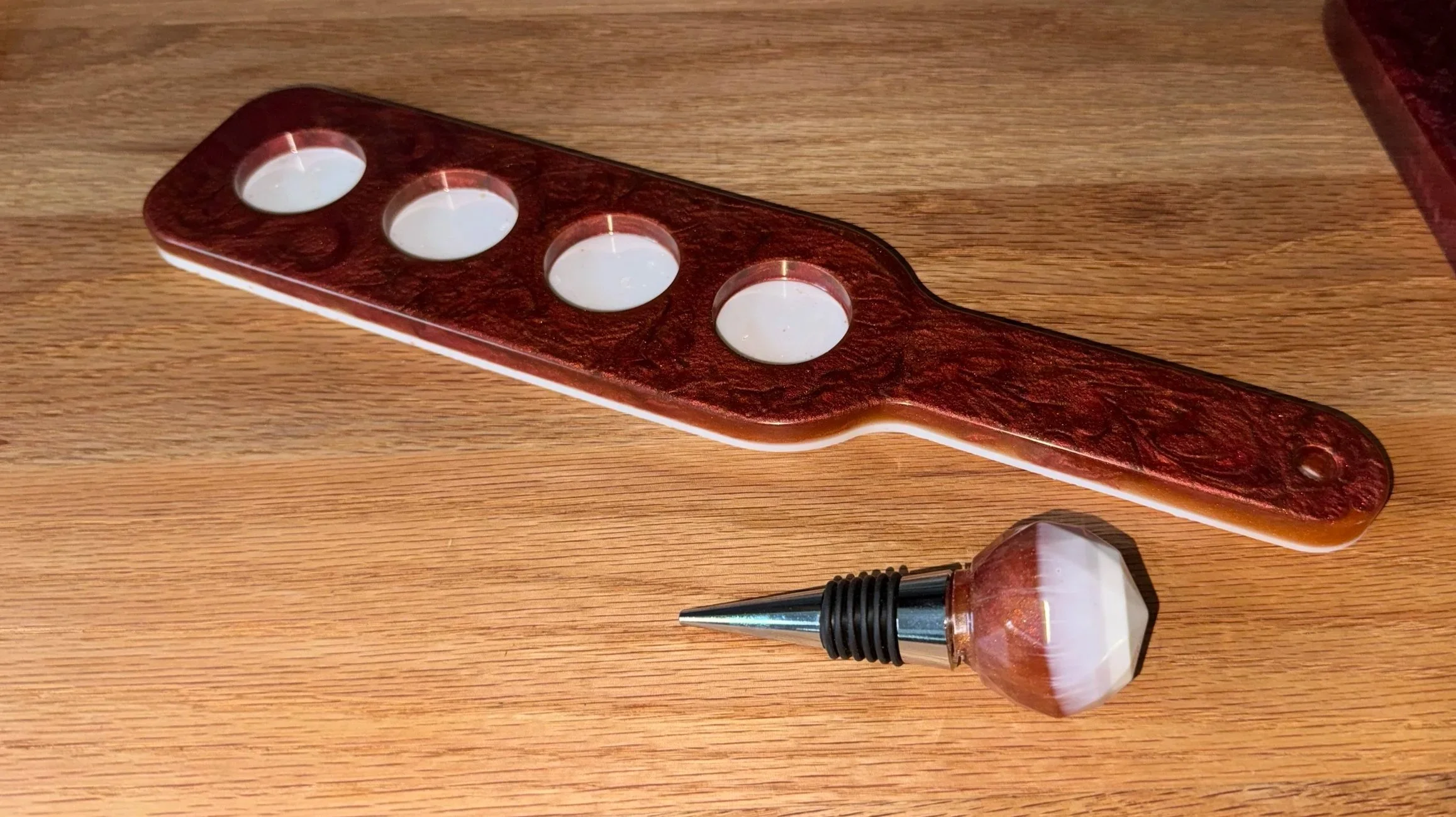 A wooden table holds a decorative candle holder with four white tealight candles and a small wine bottle-shaped container filled with rose-colored liquid, and a pen with a smoky grey and black grip.