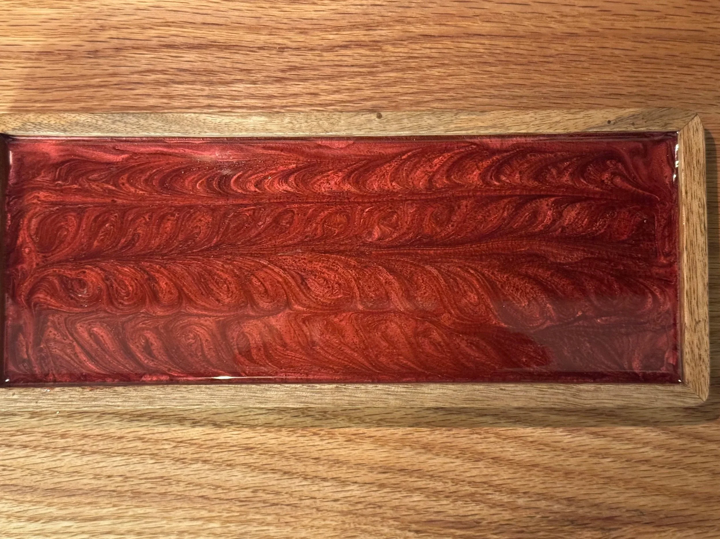 A rectangular red marble-patterned tray with a swirling design, bordered by a wooden frame, placed on a wooden surface.