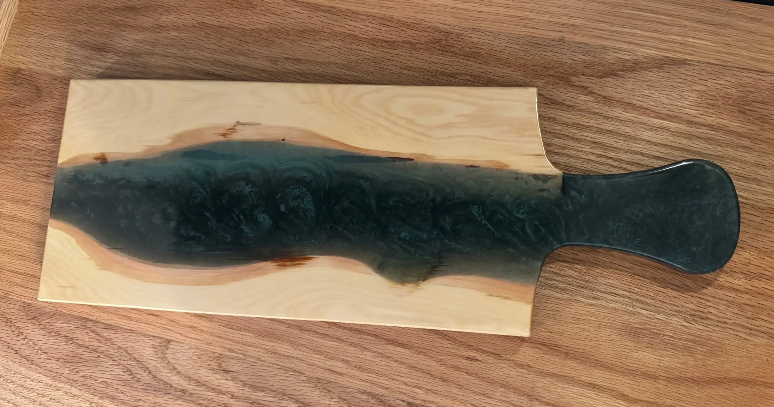 A decorative wood and resin chopping board with a sea wave design, placed on a wooden surface.