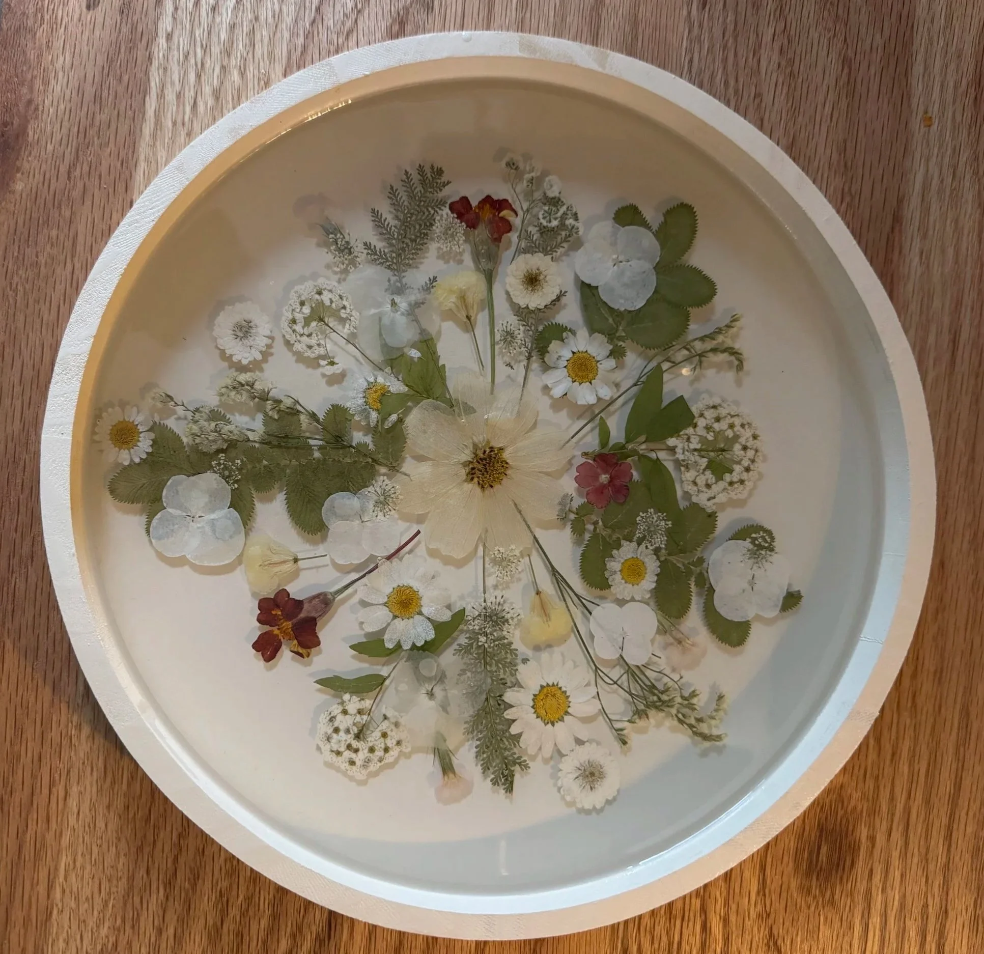 Decorative oval white tray with pressed and dried flowers floating in a clear liquid.