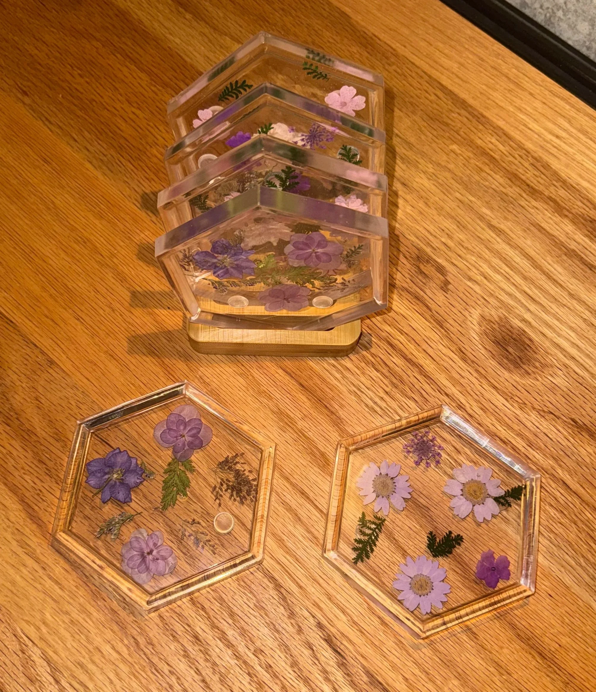 A display of four clear acrylic blocks with pressed flowers and ferns inside, arranged on a wooden surface.