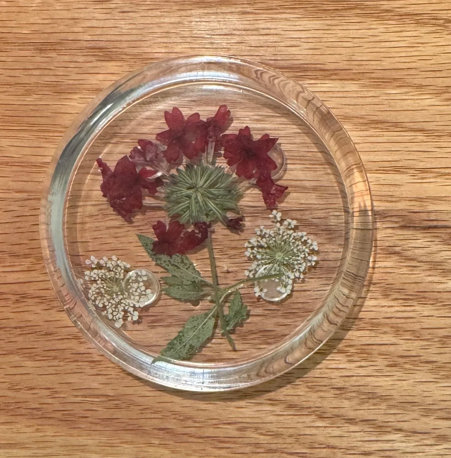 A clear glass dish with pressed flowers inside, placed on a wooden surface.