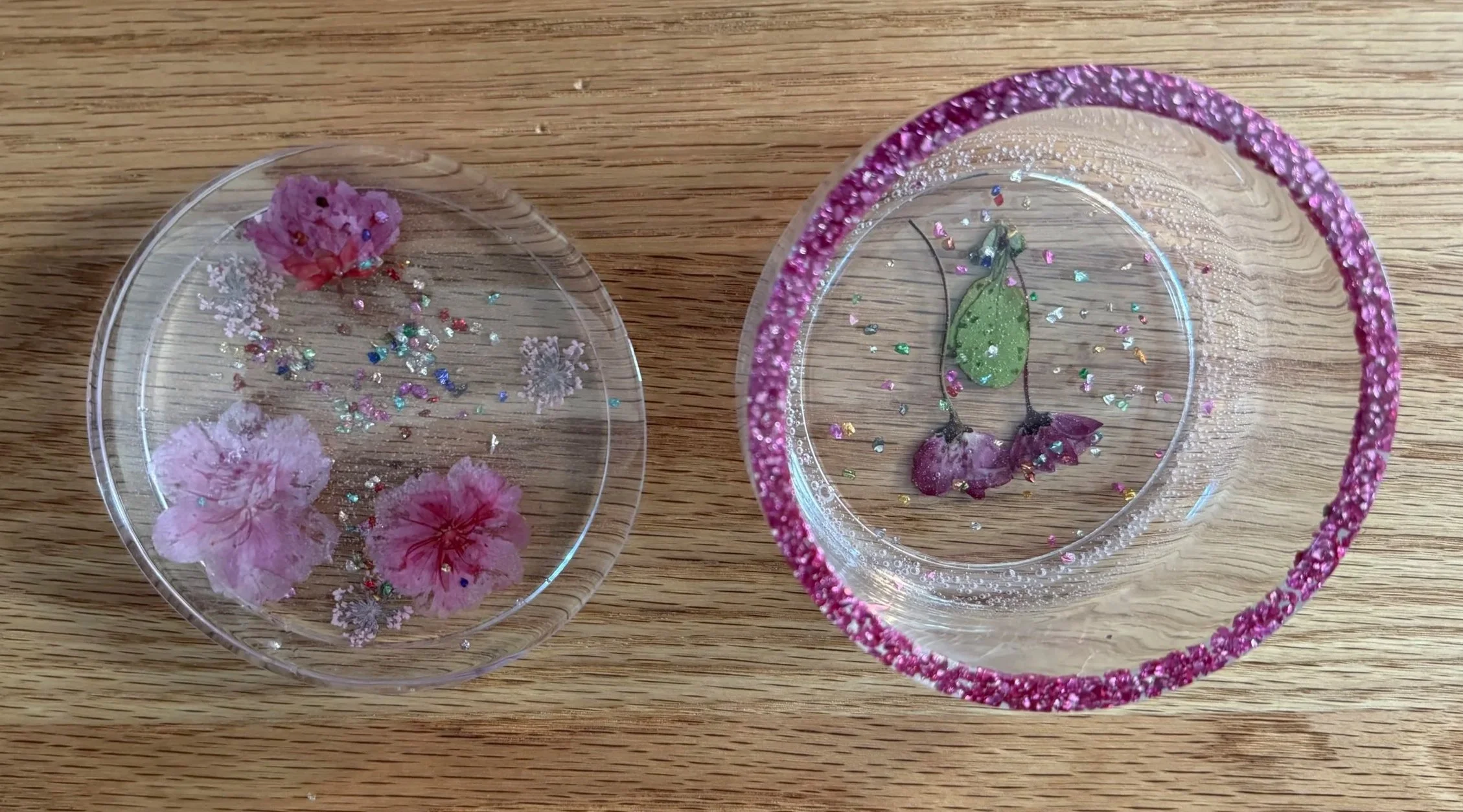 Two clear plastic containers with pink and purple flower designs and glitter, placed on a wooden surface.