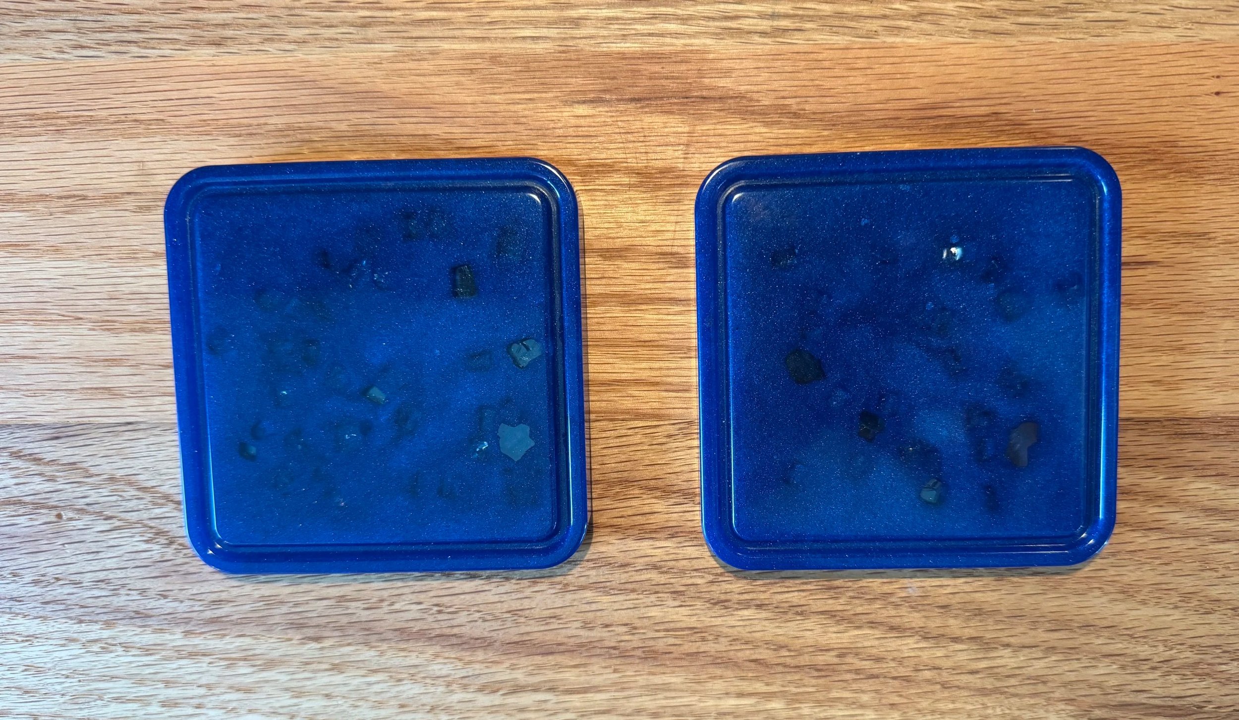 Two blue containers with small gray stones inside, placed on a wooden surface.