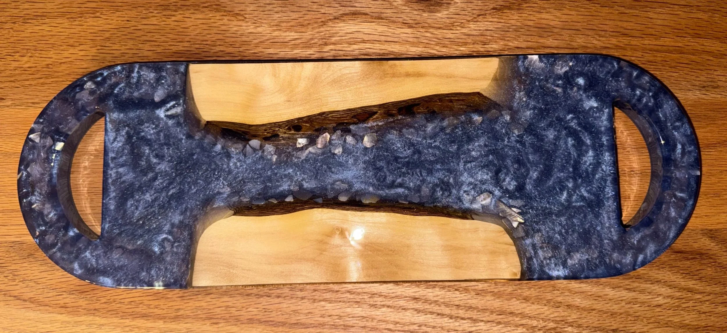 Decorative tray with a black marble-like surface and a contrasting light wood center, placed on a wooden surface.