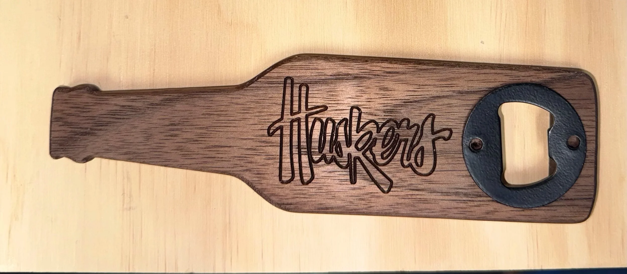 A wooden beer bottle opener with a black metal ring and Huskers engraved for football tailgates and game day.