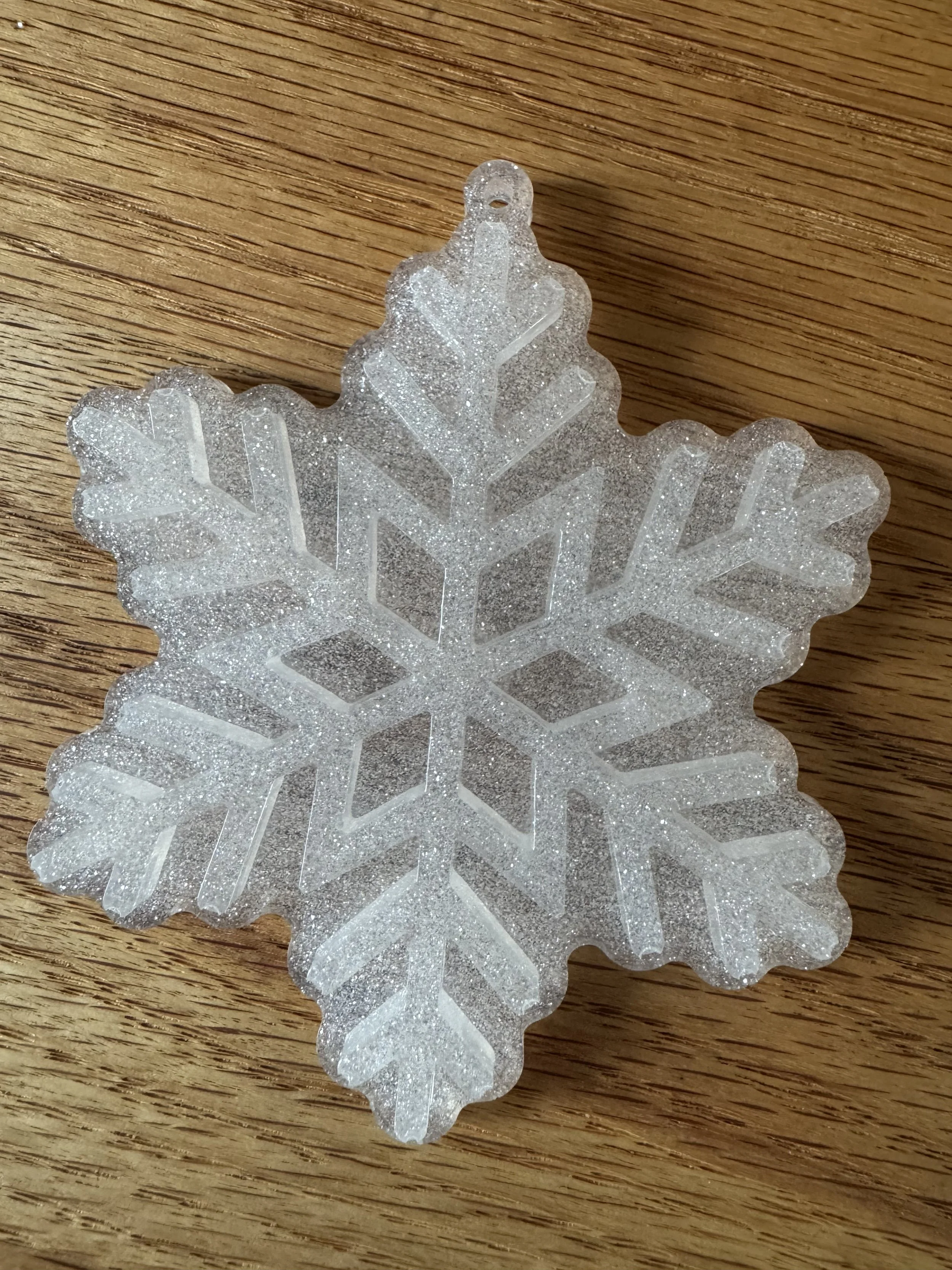 Close-up of clear shimmery resin snowflake ornament/decoration with glitter, resting on a wooden surface.