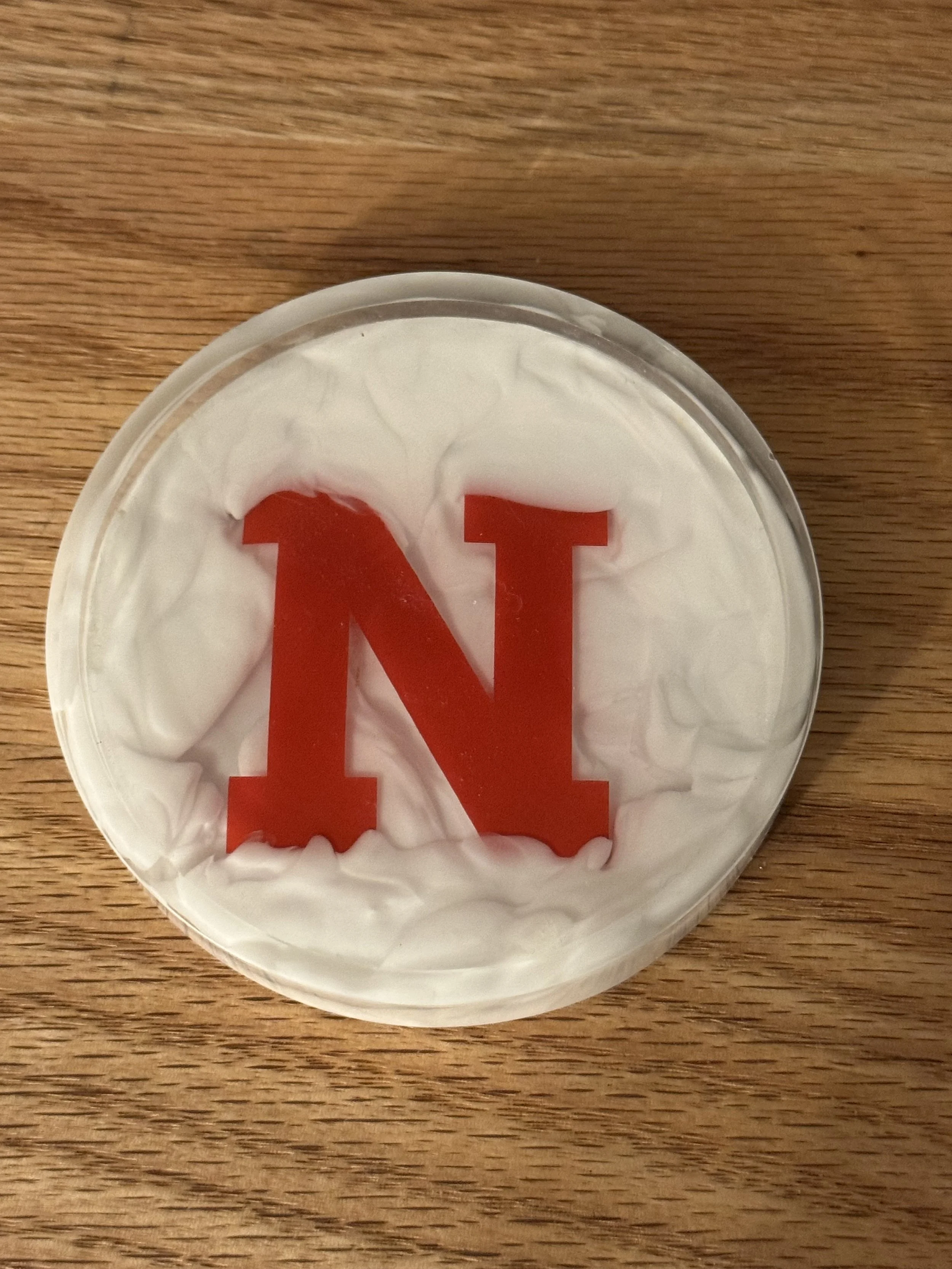A container of white yogurt with a large red letter 'N' on the surface, placed on a wooden surface.