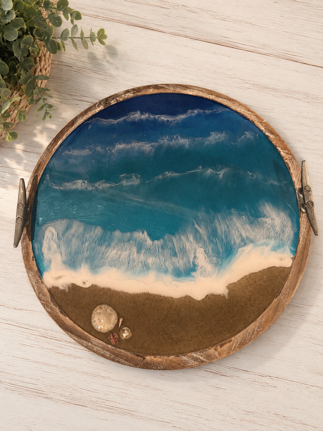 Seaside resin scene with blue ocean waves crashing onto a sandy shore, with seashells on the sand, inside a round wooden decorative tray.