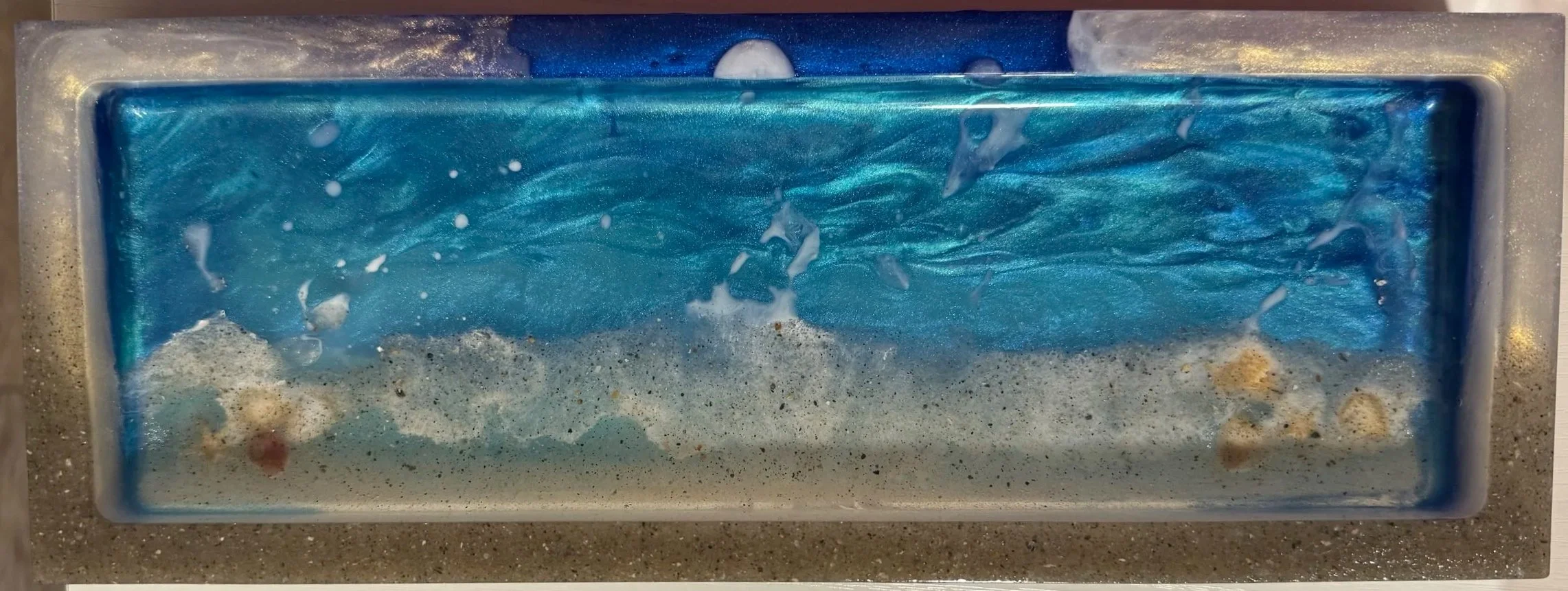 A rectangular container filled with swirling blue, white, and beige soap foam and bubbles, resembling ocean waves.