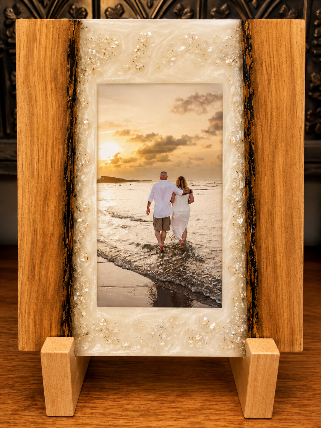 A wood and resin photo frame with a decorative seashell border, containing a picture of a couple embedded in resin walking along the beach at sunset.