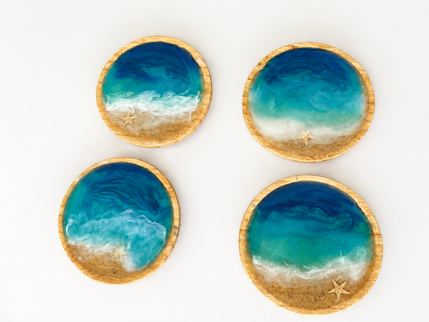 Four round decorative plates with ocean wave designs, starfish accents, set against a white background.