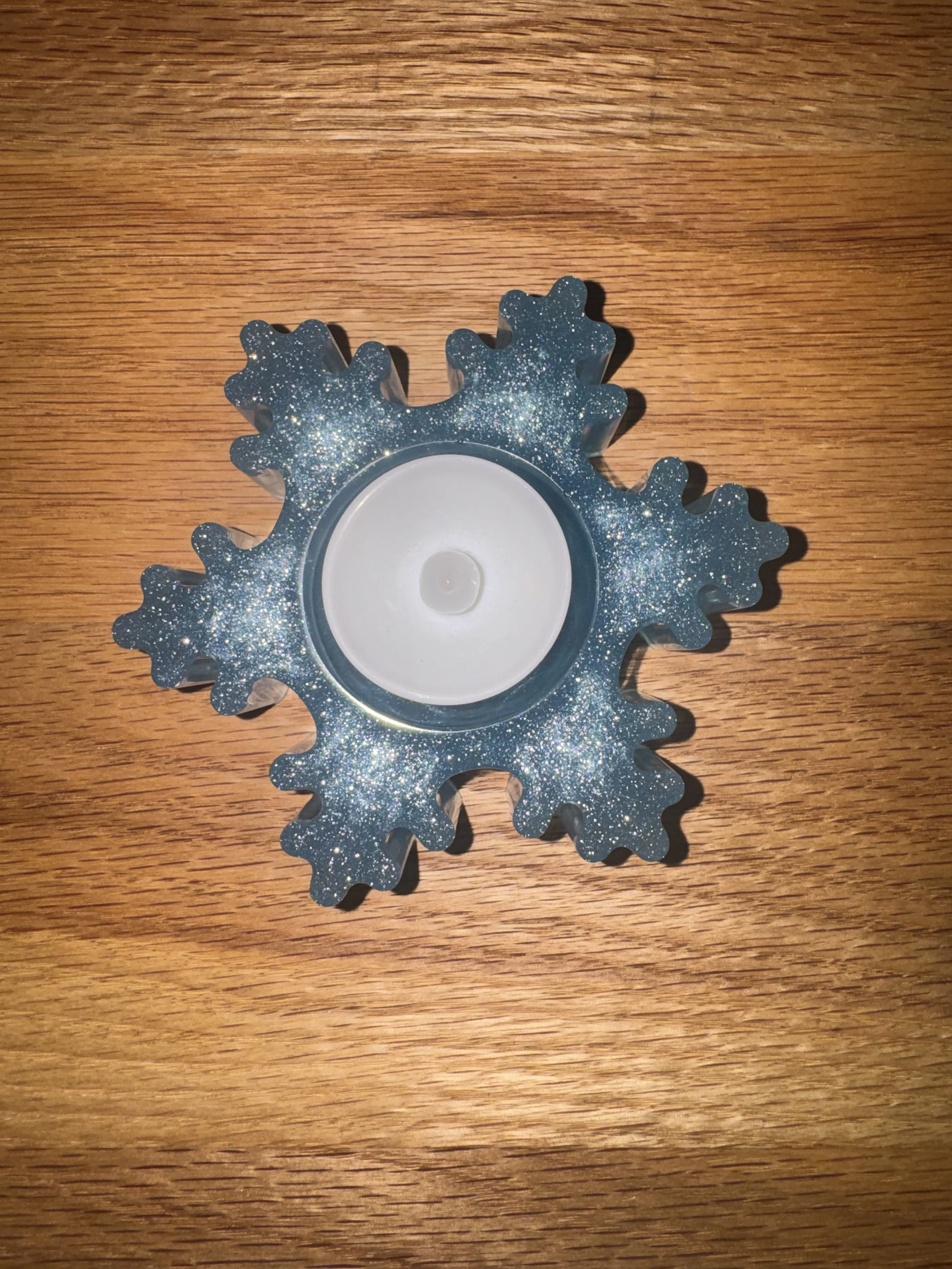 A glittery blue resin snowflake-shaped tealight candle holder on a wooden surface.