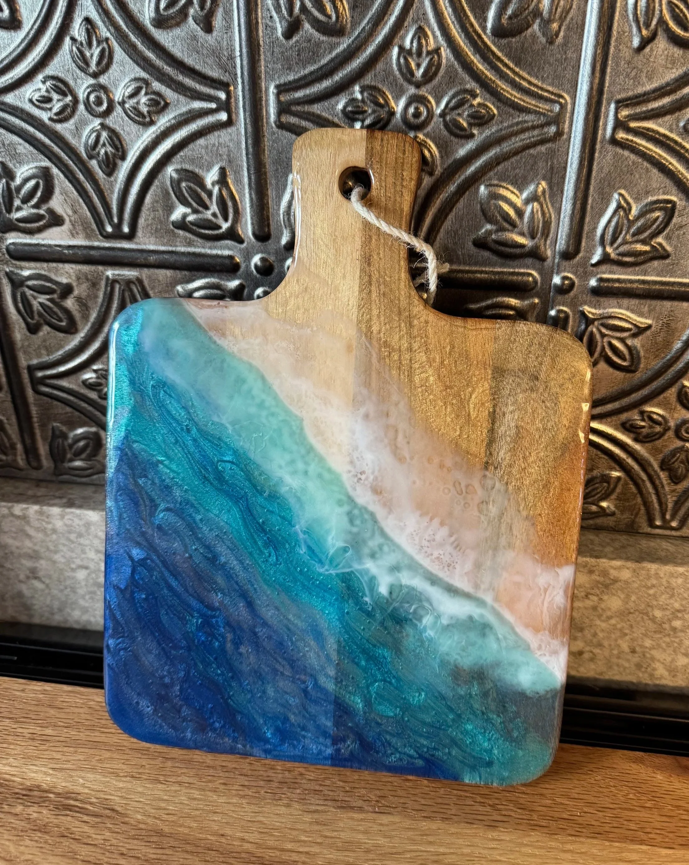 A decorative piece of art wood and resin, featuring abstract swirling patterns in shades of blue, white, and natural wood color, placed on a wooden surface.
