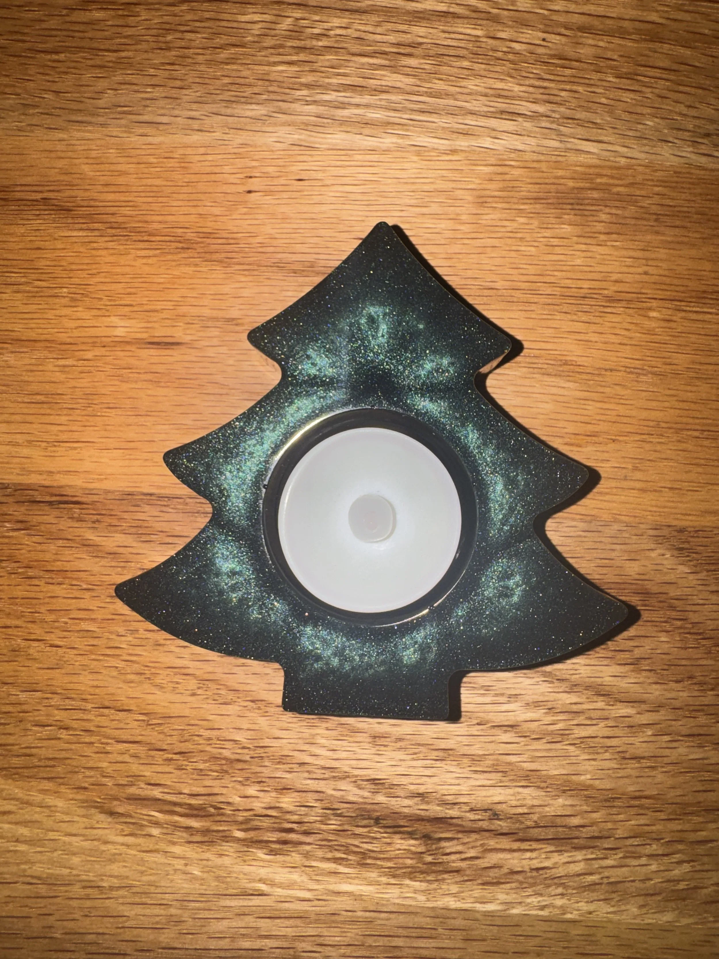 A small decorative resinChristmas tree with a swirled pattern, positioned on a wooden surface.