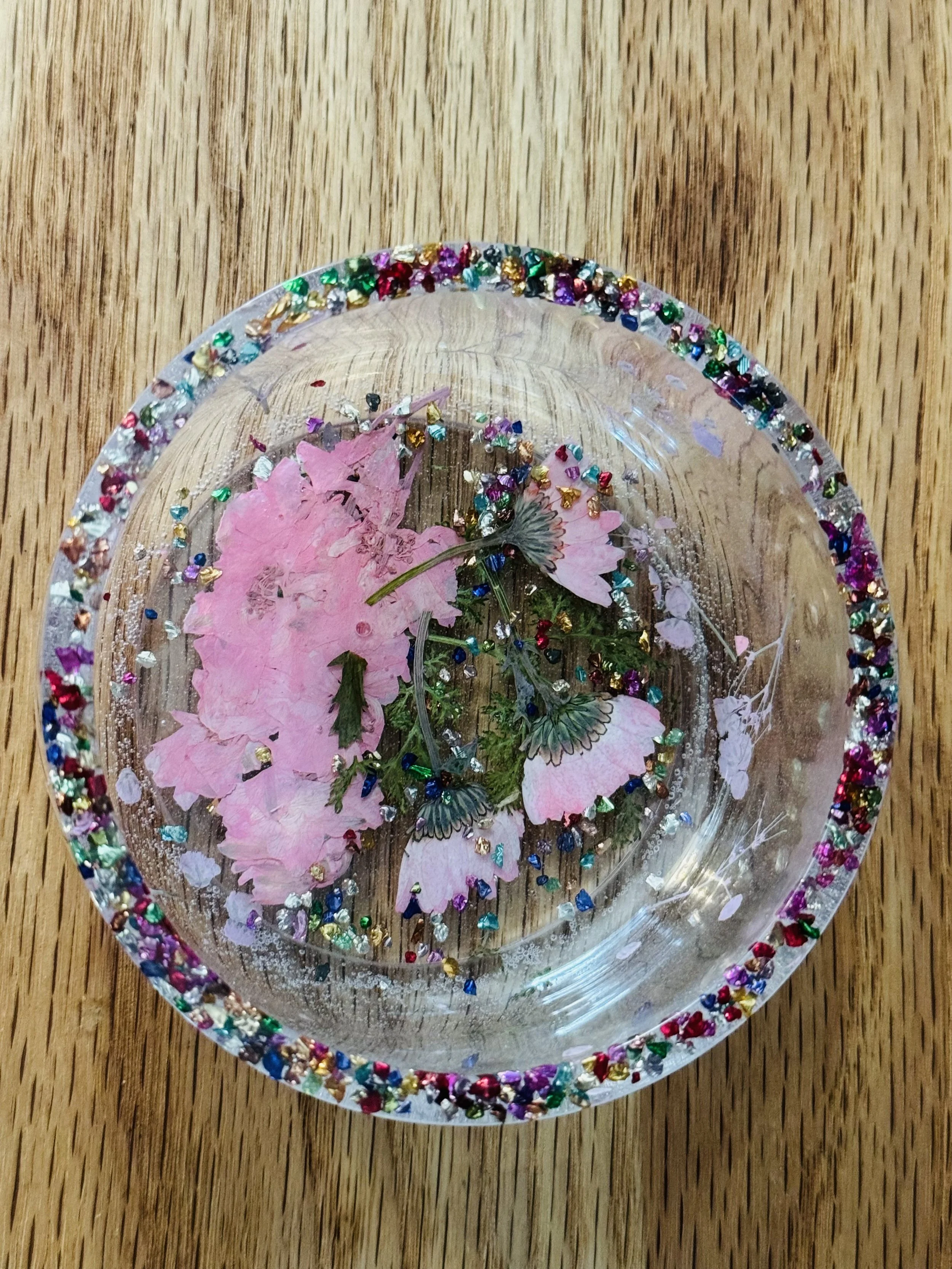 Decorative glass bowl with pink flowers and colorful glitter on a wooden surface.