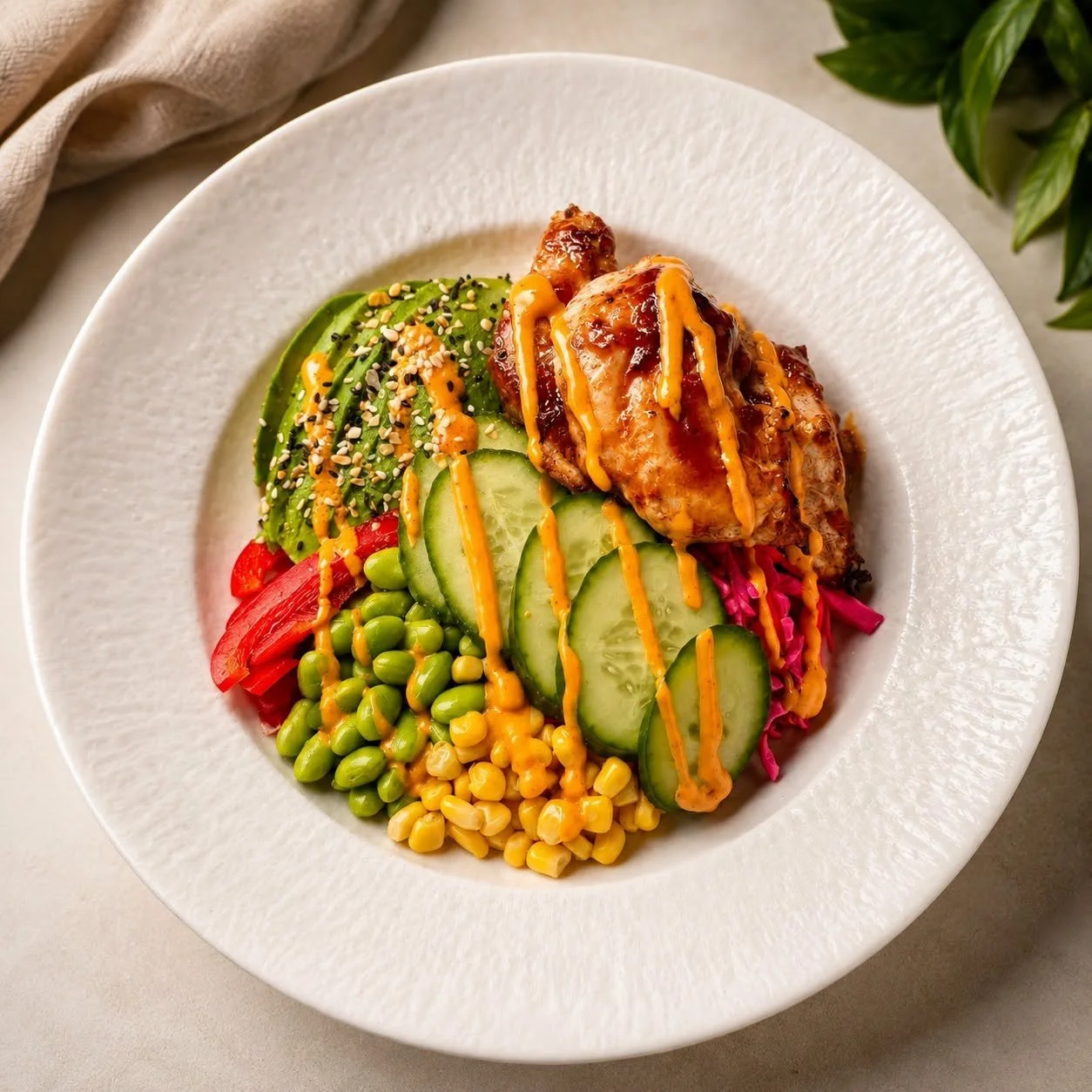 A white plate with a salad containing sliced cucumbers, shredded red cabbage, green peas, corn, sliced avocado, and slices of red bell pepper, topped with a grilled chicken thigh drizzled with a yellow sauce.
