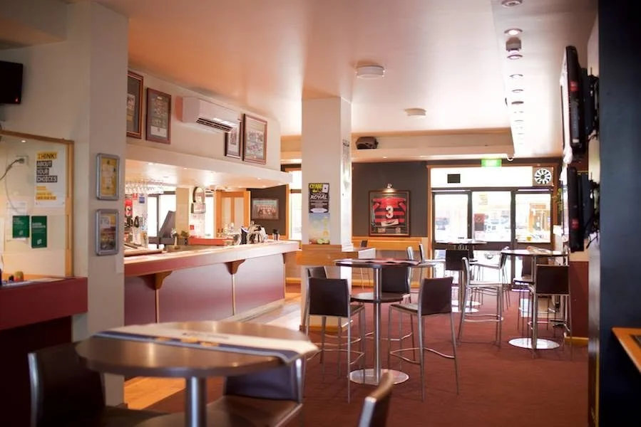 Inside a quiet sports bar with tables, chairs, a counter area, and flat-screen TVs on the wall, near the entrance.