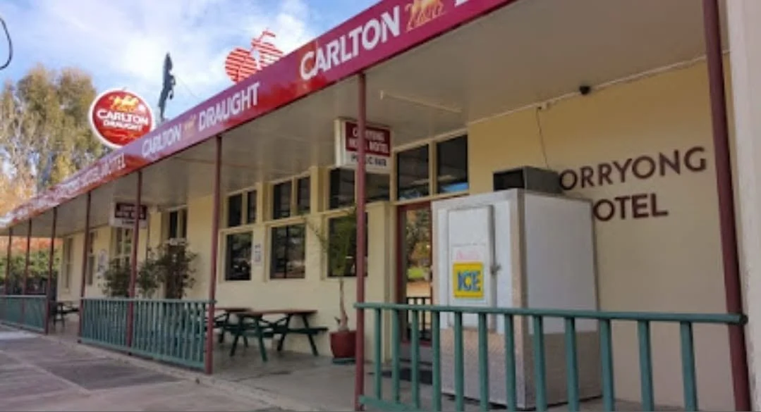 Front view of a motel with signs for Carlton Draught beer, picnic tables, and an ice vending machine outside.