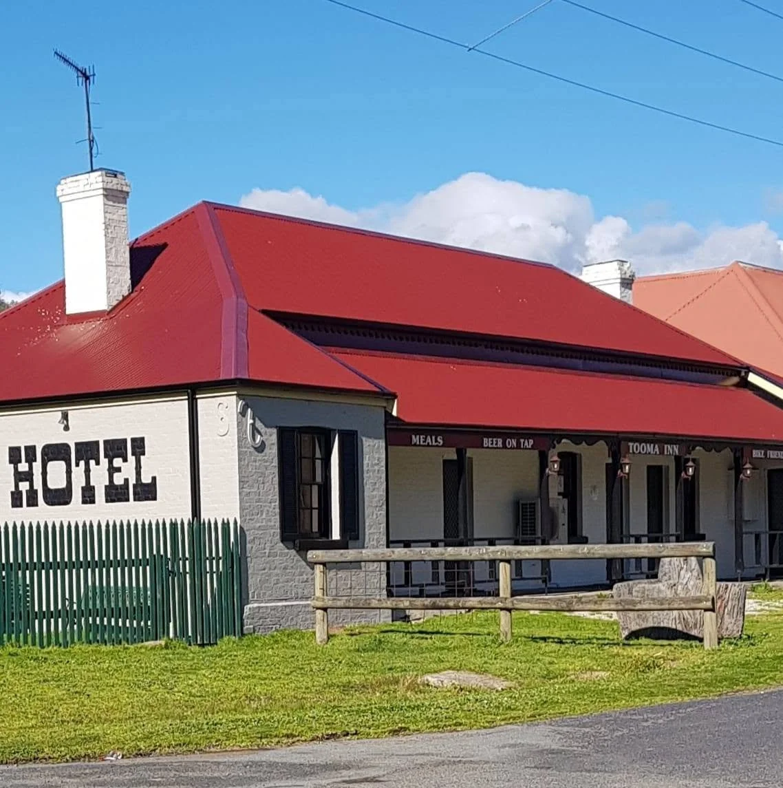 A building with a red roof and white brick walls, labeled as a hotel, with a porch and signs indicating it offers meals and beer on tap.