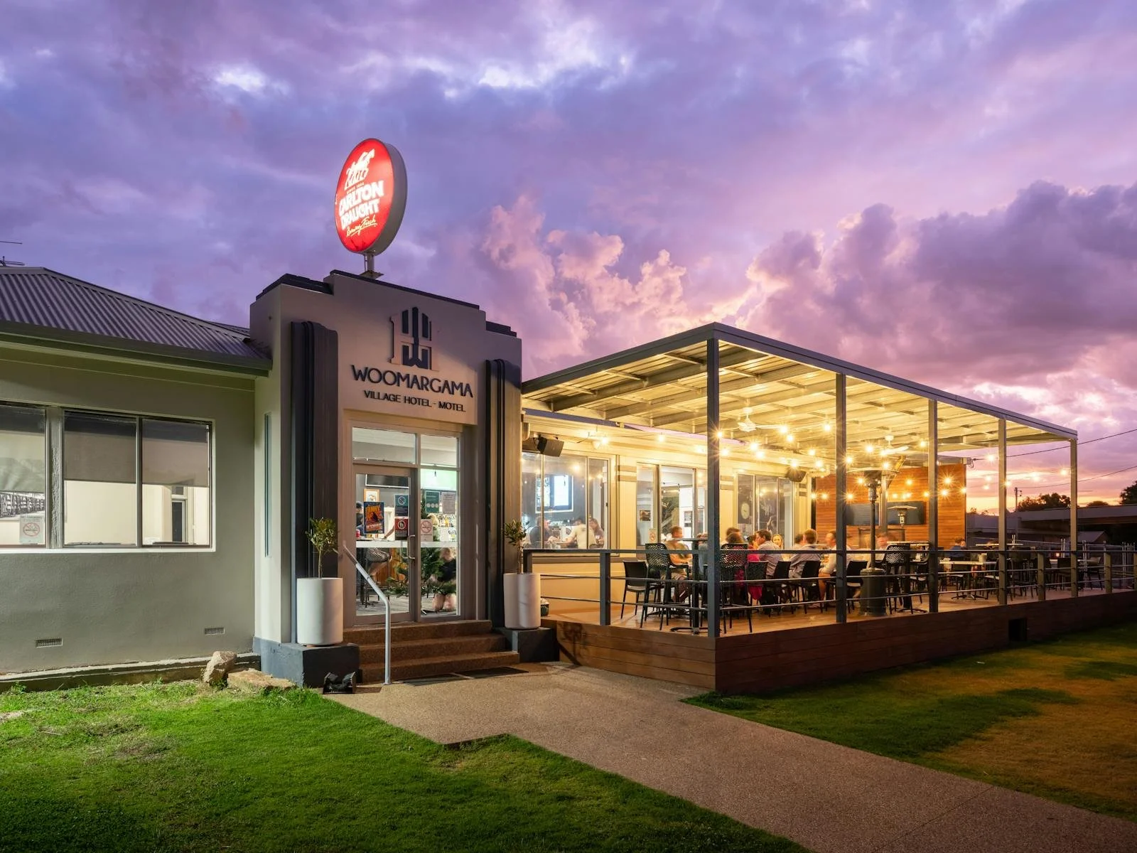 Exterior of Woomargama Village Hotel motel with outdoor dining area illuminated at dusk, purple sky with clouds in the background
