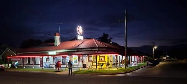 Nighttime view of a fast-food restaurant with a red roof, illuminated sign, and people outside.