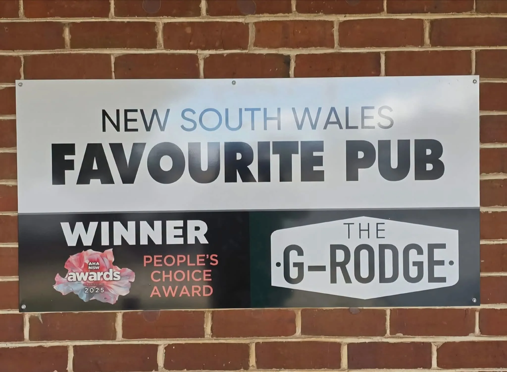 A sign on a brick wall promoting a pub as a favorite in South Wales, with partial advertisements for awards and a G-Rodge award.