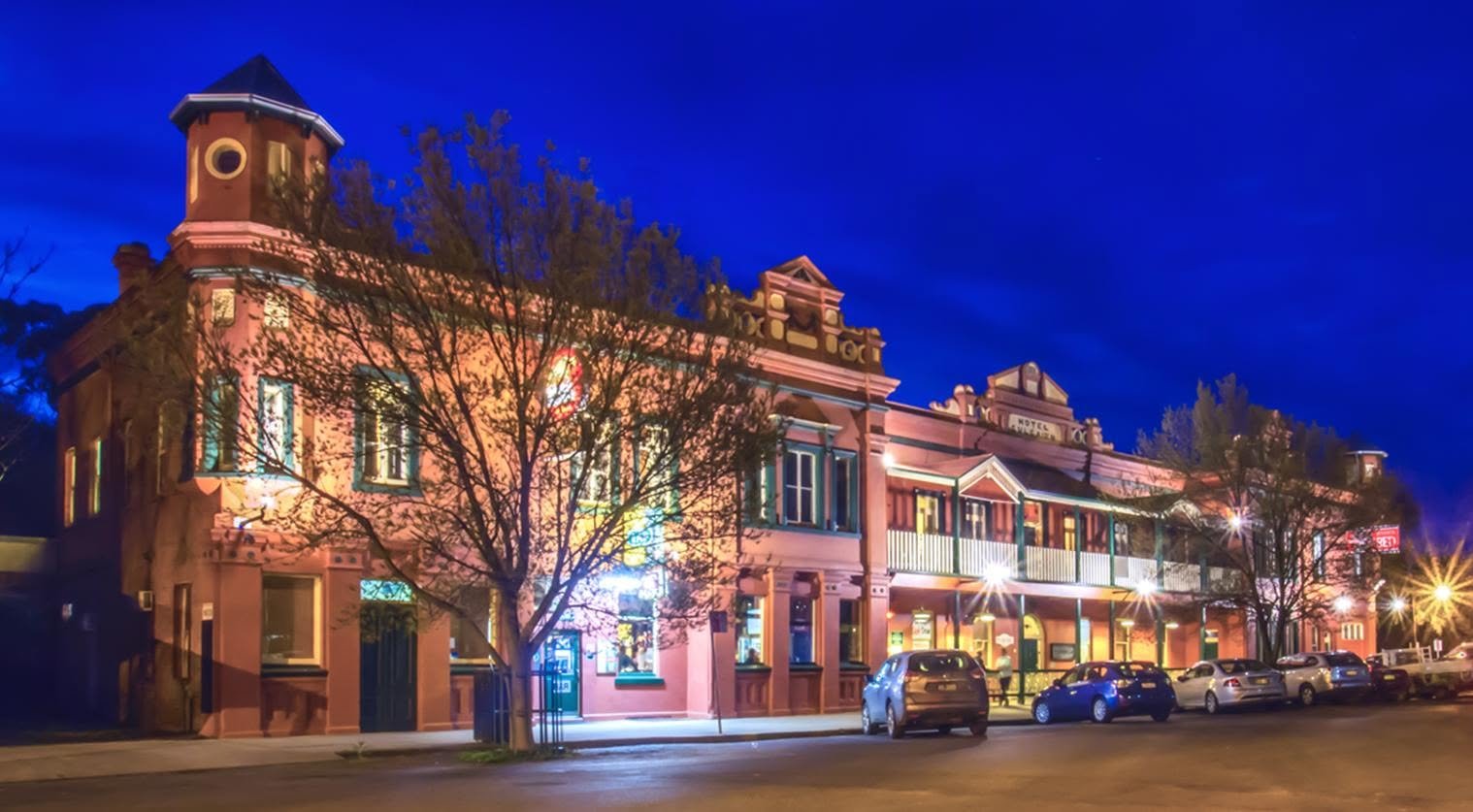 A brightly lit historic hotel building at night, with colorful exterior lights and parked cars in front.