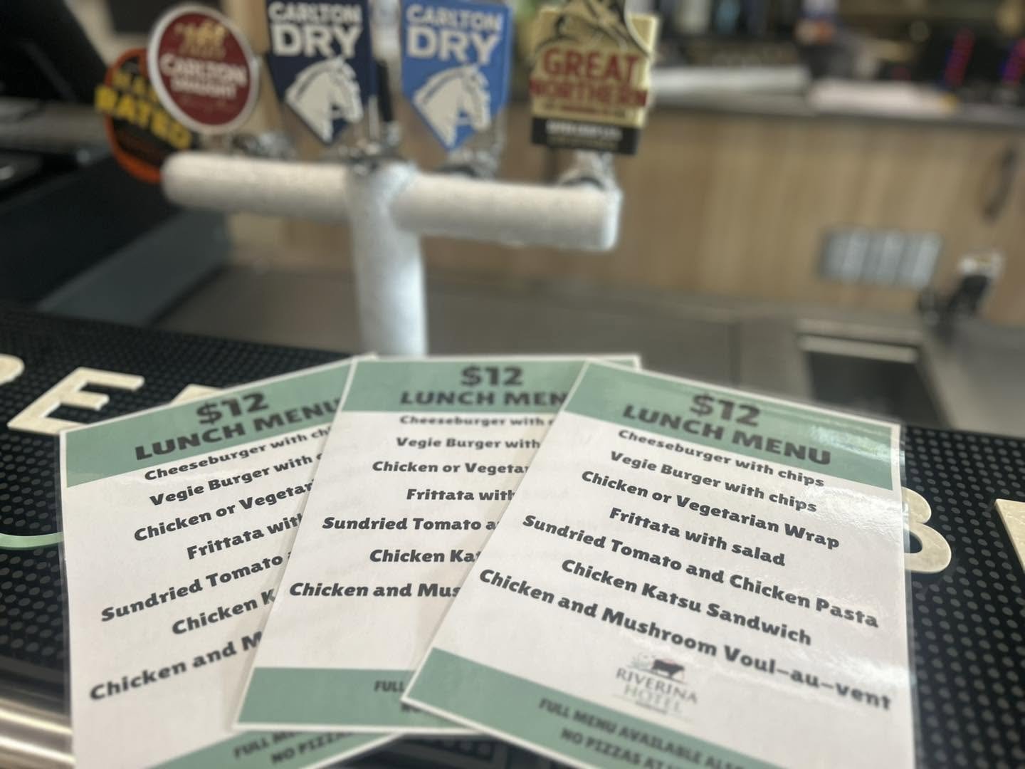 Three $12 lunch menu cards for a restaurant, listing cheeseburger with chips, veggie burger with chips, chicken or vegetarian wrap, fritata with salad, sundried tomato and chicken pasta, chicken katsu sandwich, and chicken and mushroom vol-au-vent.