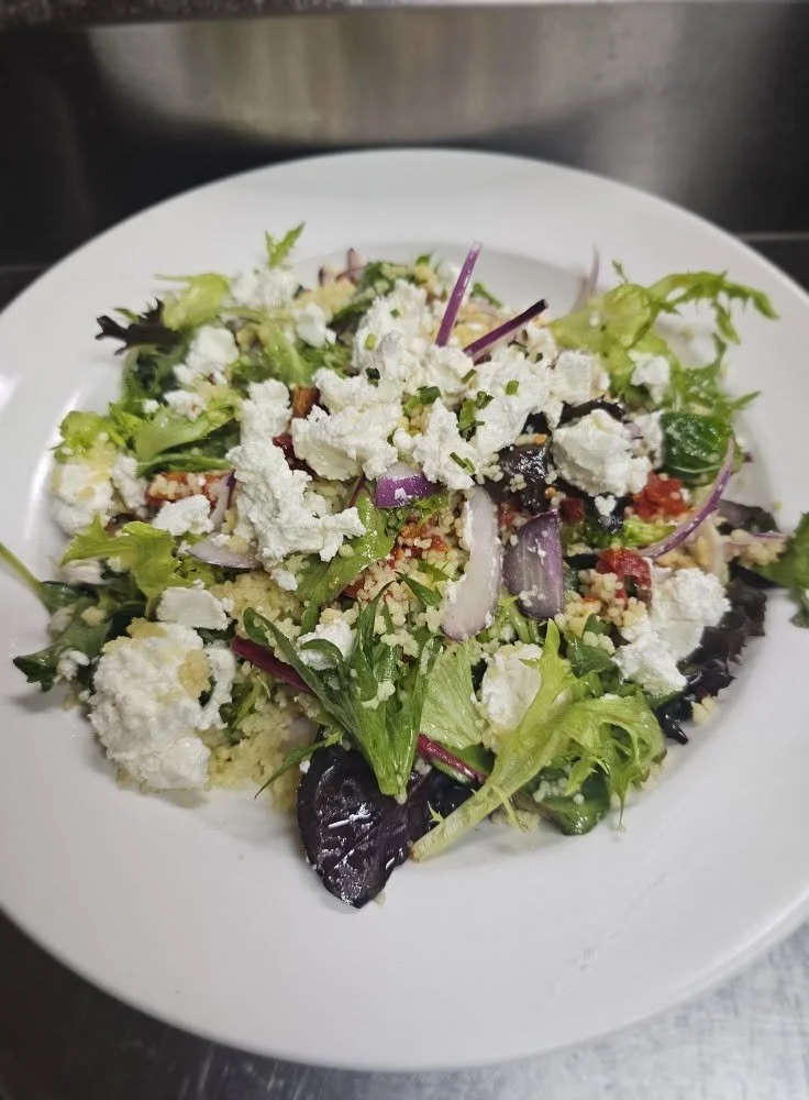 Mixed green salad with crumbled white cheese, red onion slices, and chopped vegetables on a white plate.