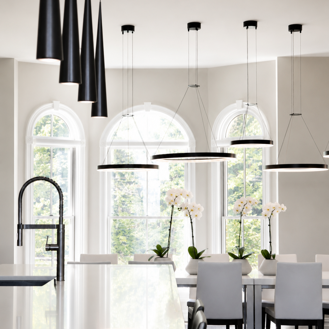 Modern kitchen with black pendant and circular pendant lights, white countertops, large arched windows, and white orchid plants in white pots.
