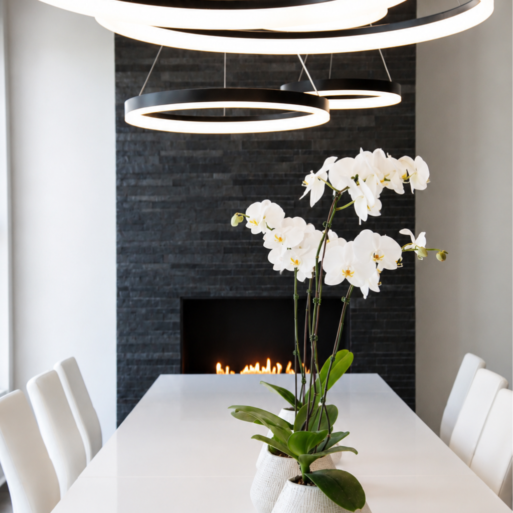 White orchid flowers in white pots on a dining table in a modern room with a black stone fireplace and circular ceiling lights.