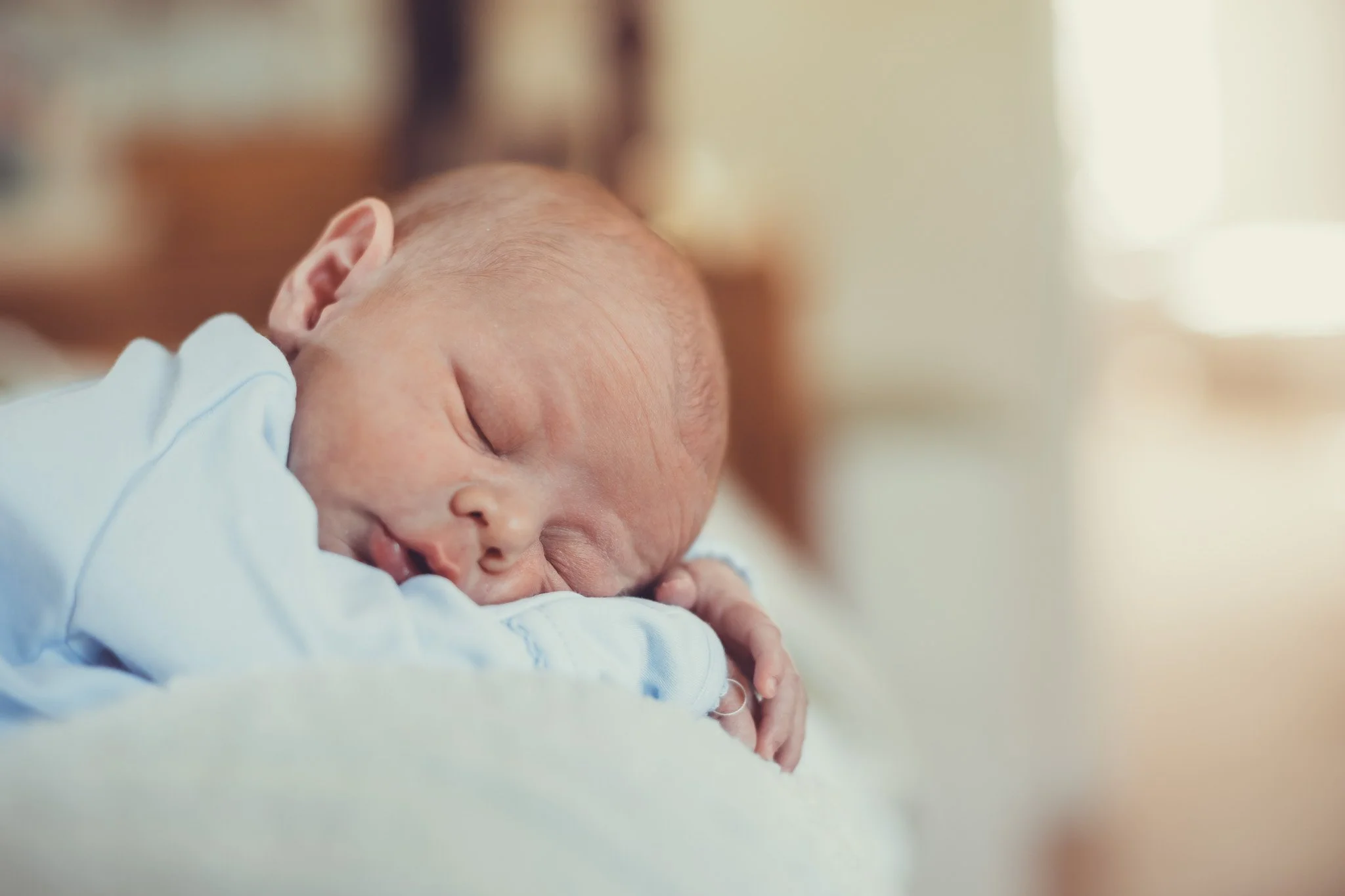 Close-up of a sleeping newborn baby with a peaceful expression, resting on a white blanket.