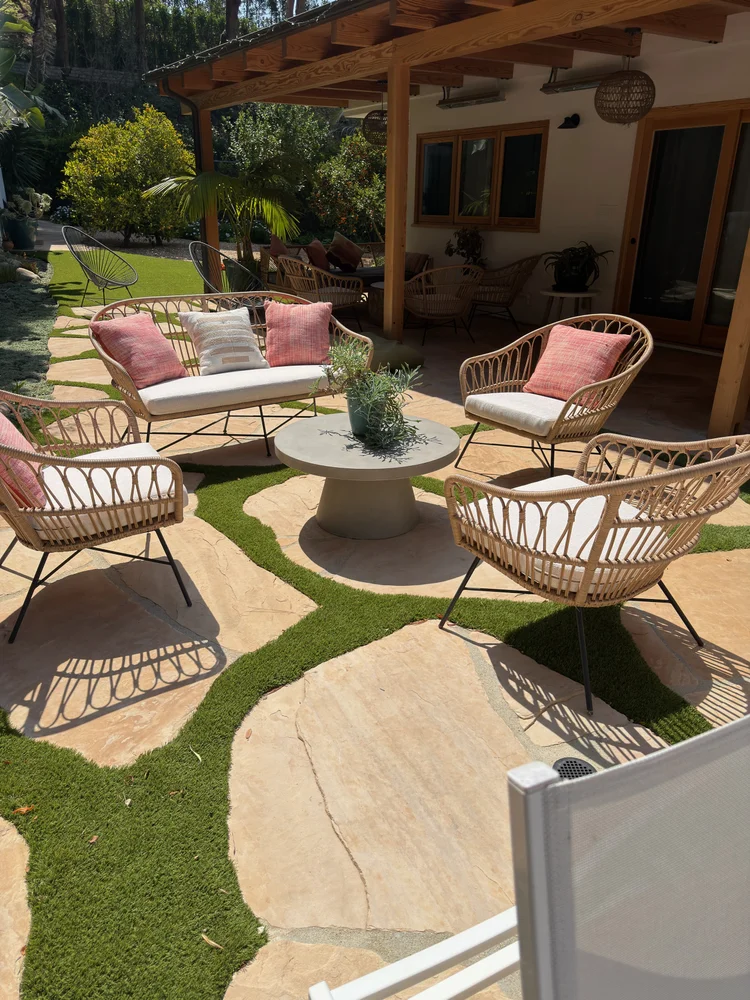 Woven outdoor patio chairs and sofa with custom fitted seat cushions and colorful throw pillows arranged around a round table in a landscaped backyard