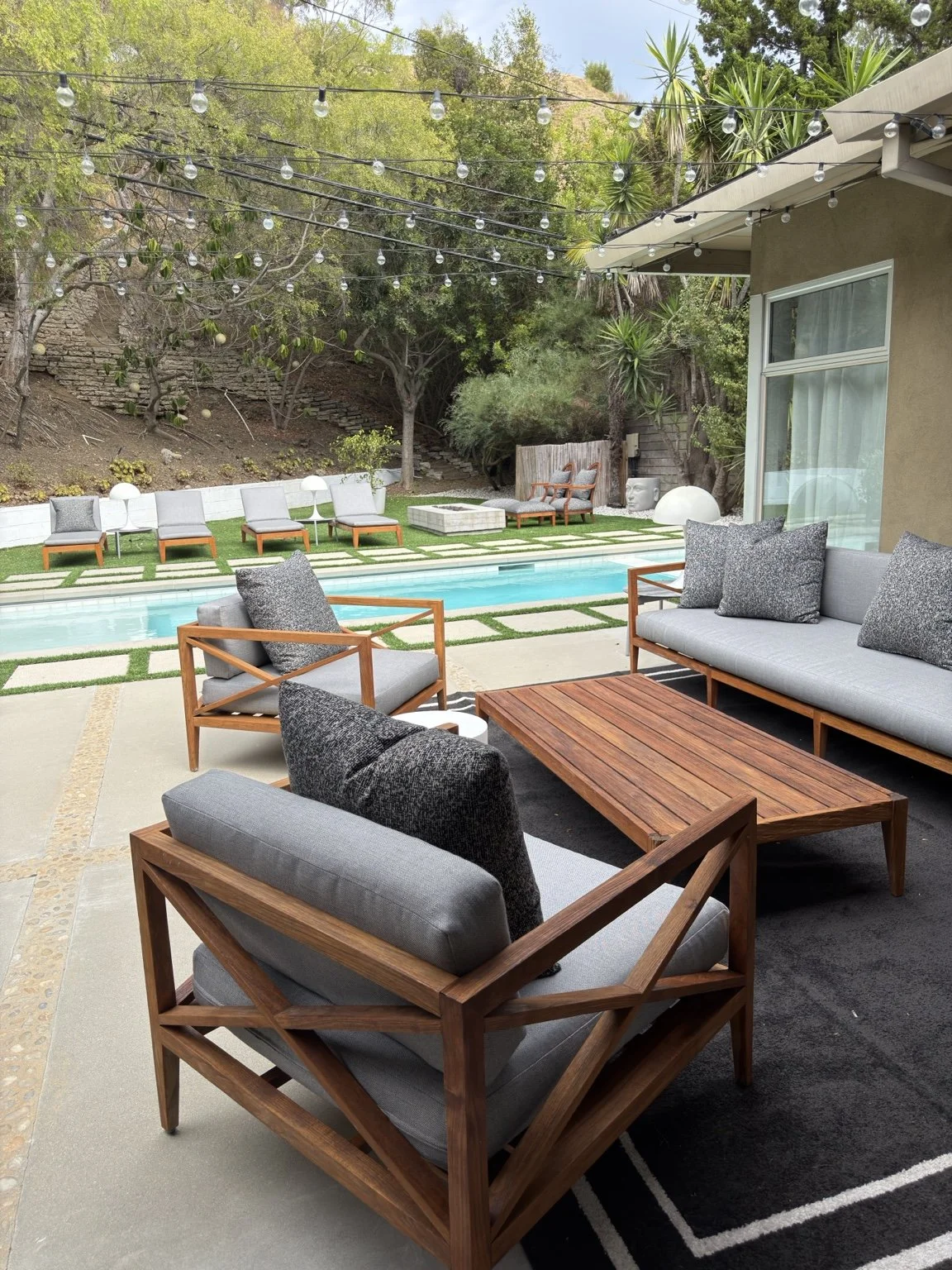 Restored teak sofa chairs and coffee table arranged beside a backyard pool