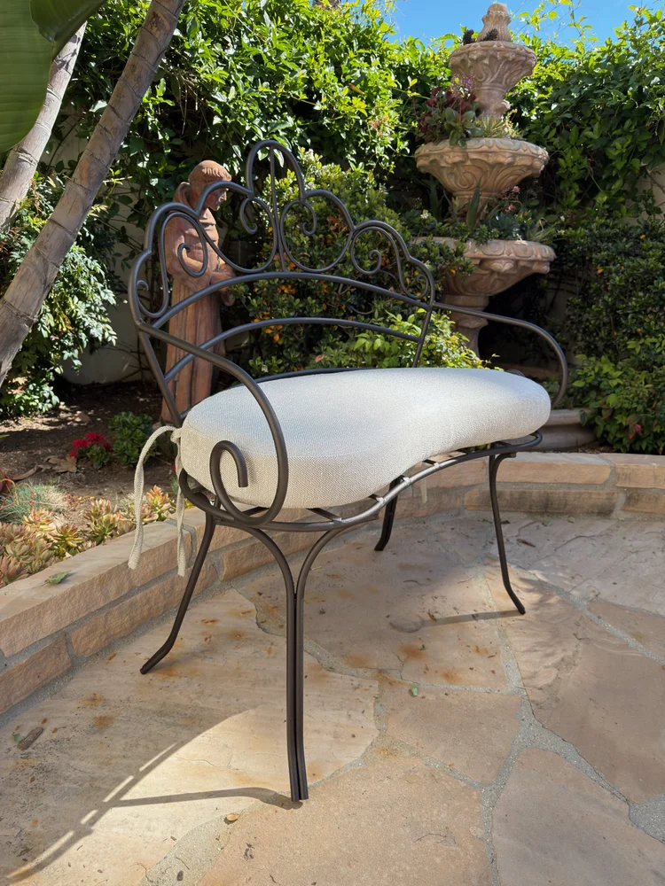 Ornate wrought iron patio chair with a custom fitted outdoor seat cushion on a landscaped backyard patio