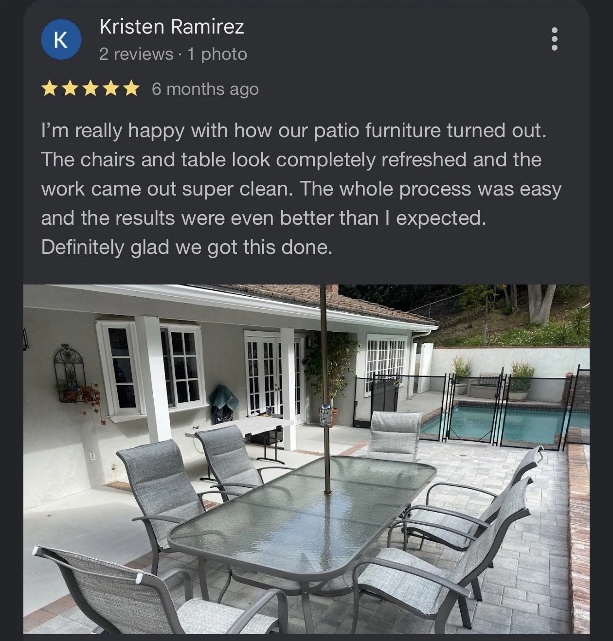 Photo of an outdoor patio area with a glass-top table, six mesh chairs, a swimming pool with a safety fence, and a white house with windows in the background.