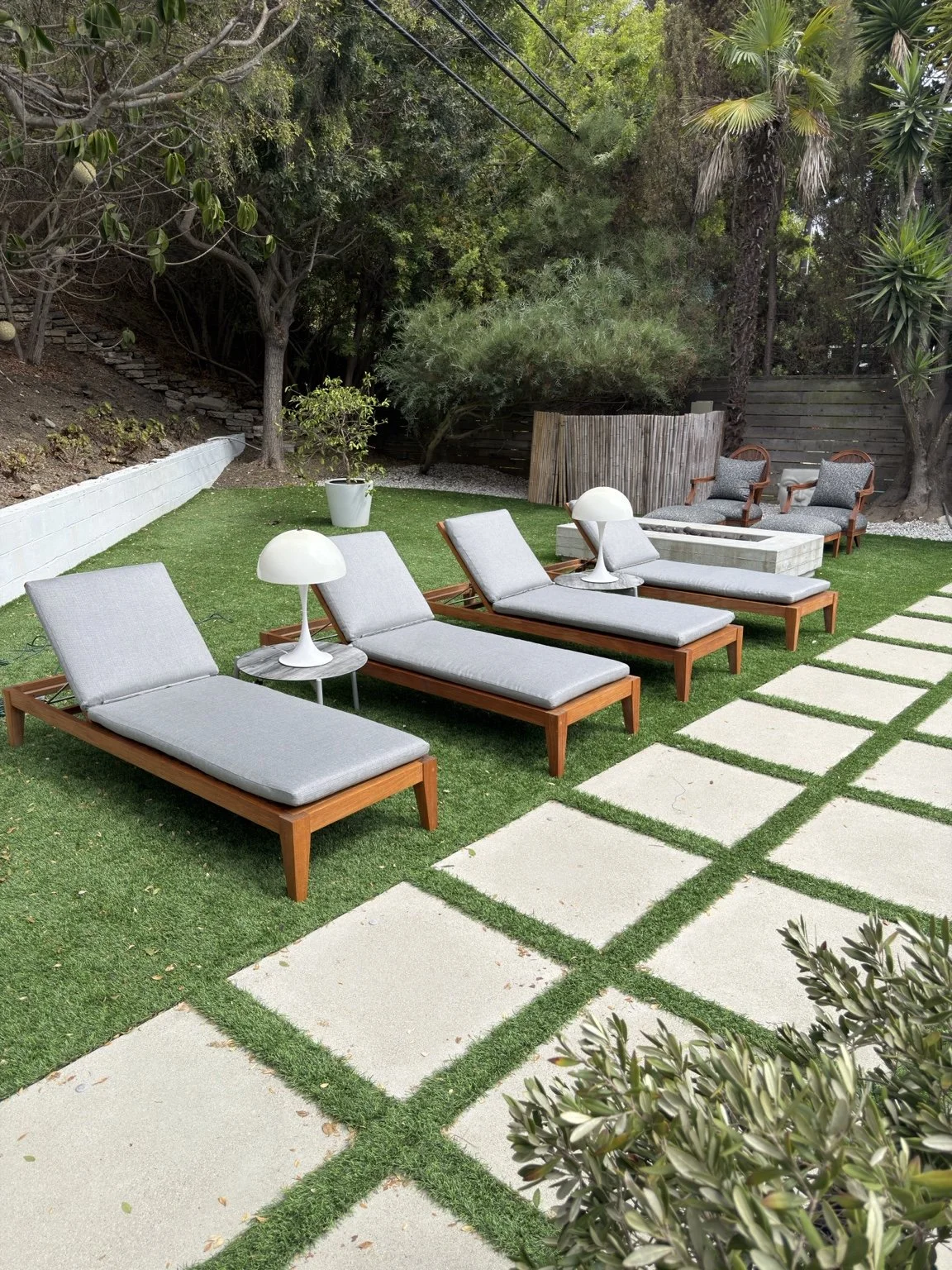 Restored teak chaise lounges with gray cushions in a landscaped backyard