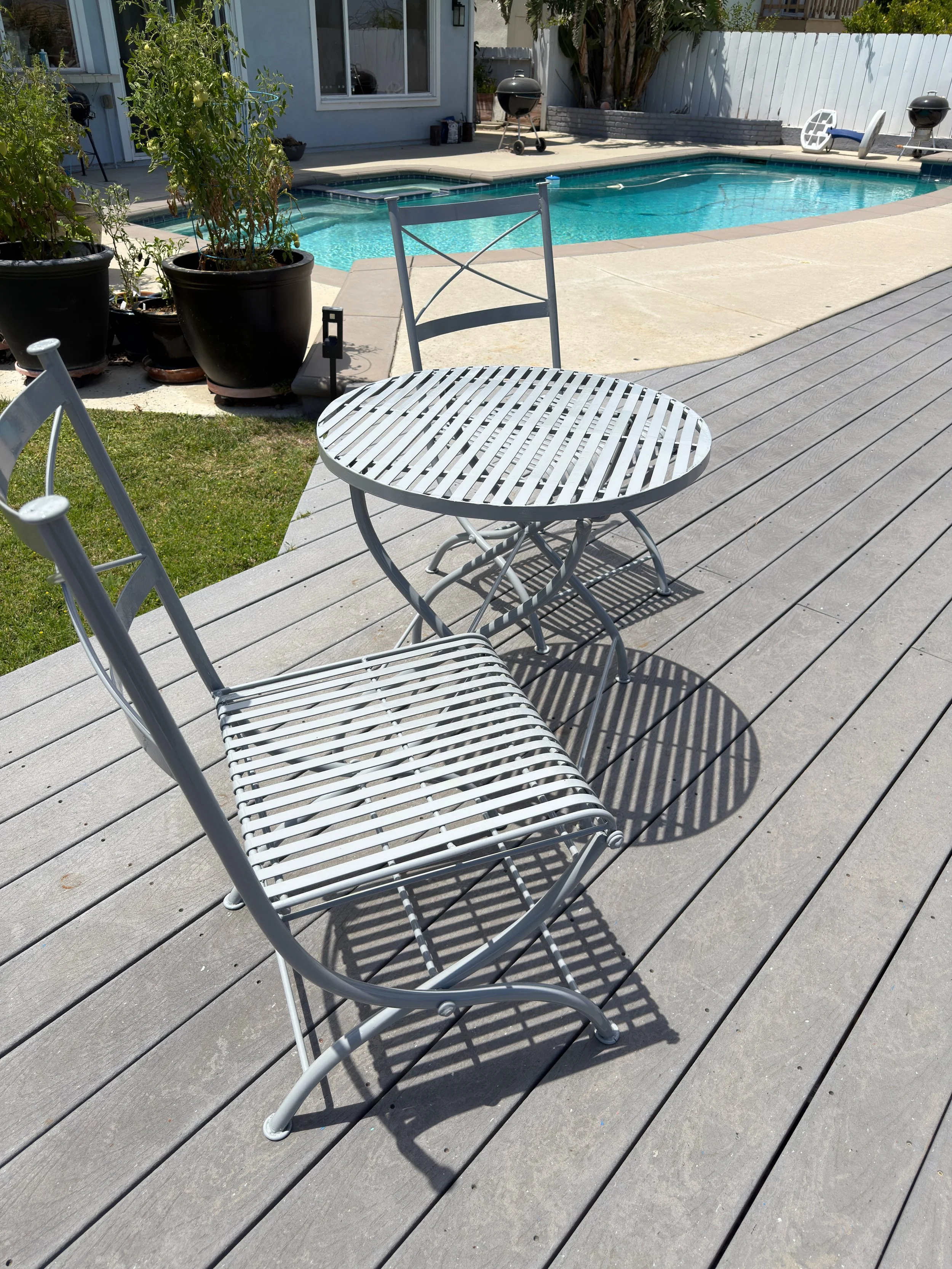 Metal patio chair and round outdoor table restored with a fresh powder coated finish on a backyard poolside deck