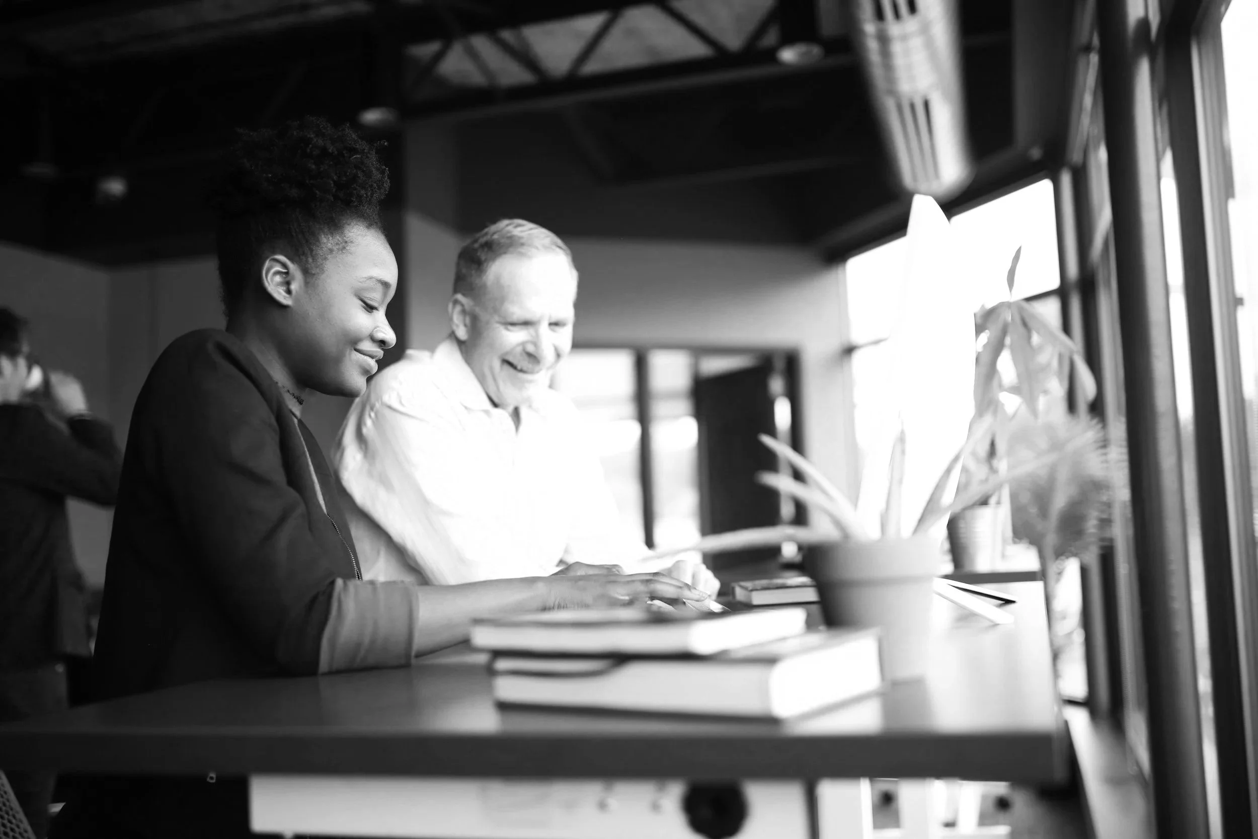 young adult African American female professional working with a older middle aged professional white male at a desk with books and a computer
