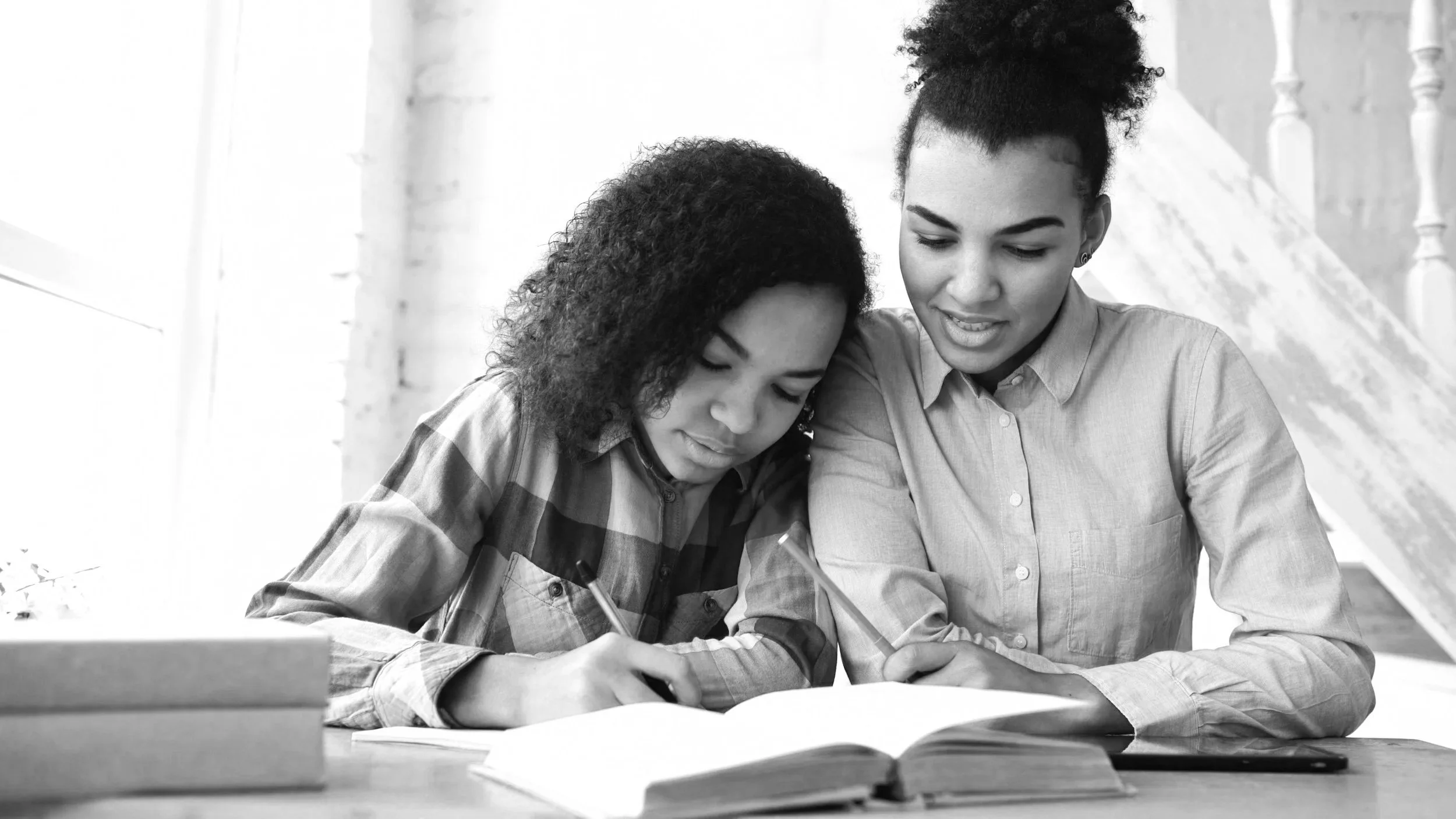 African American tutor or parent with adolescent female African American student reading a book together at a table