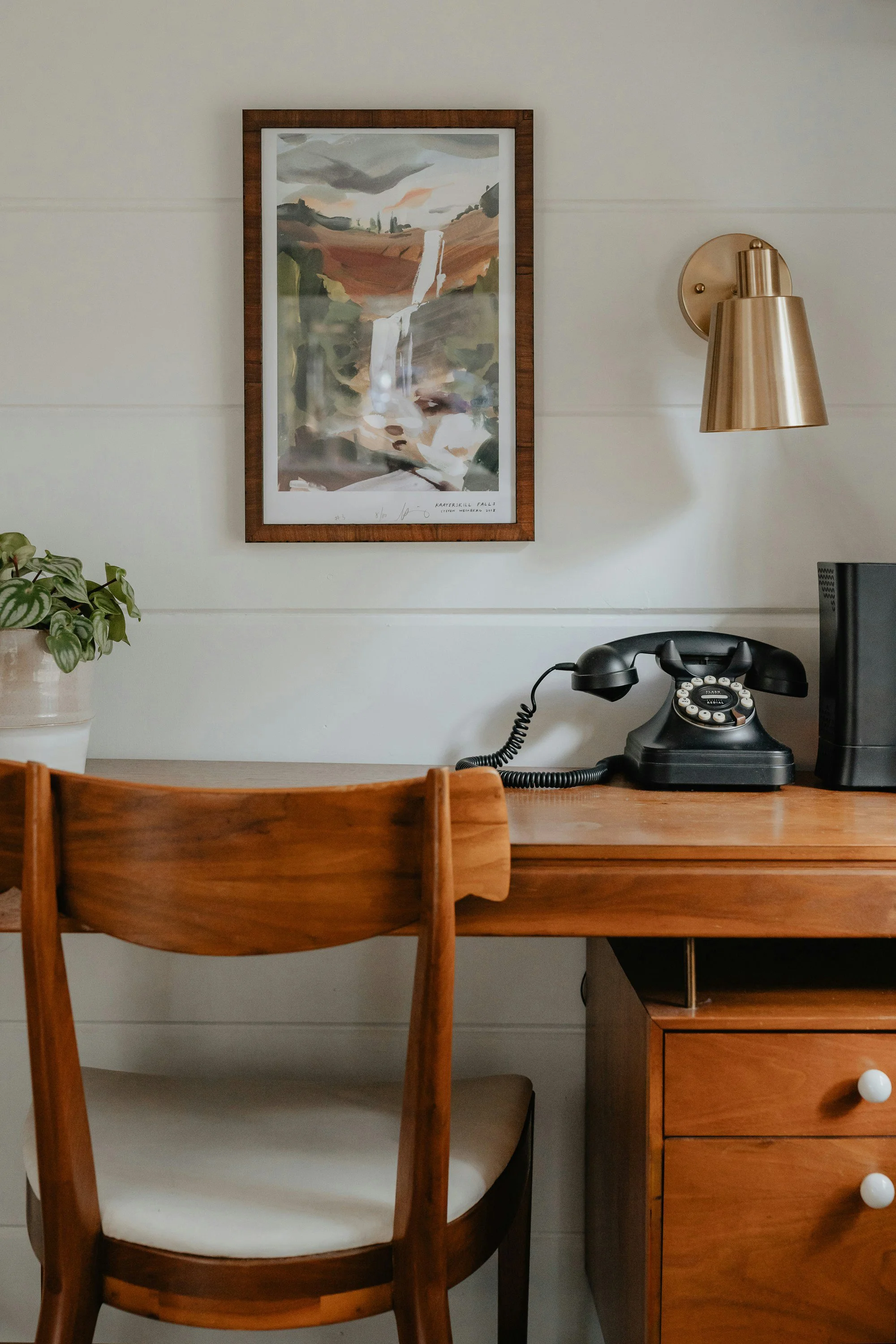 Wooden desk with a vintage landline phone, plant and art on the wall.
