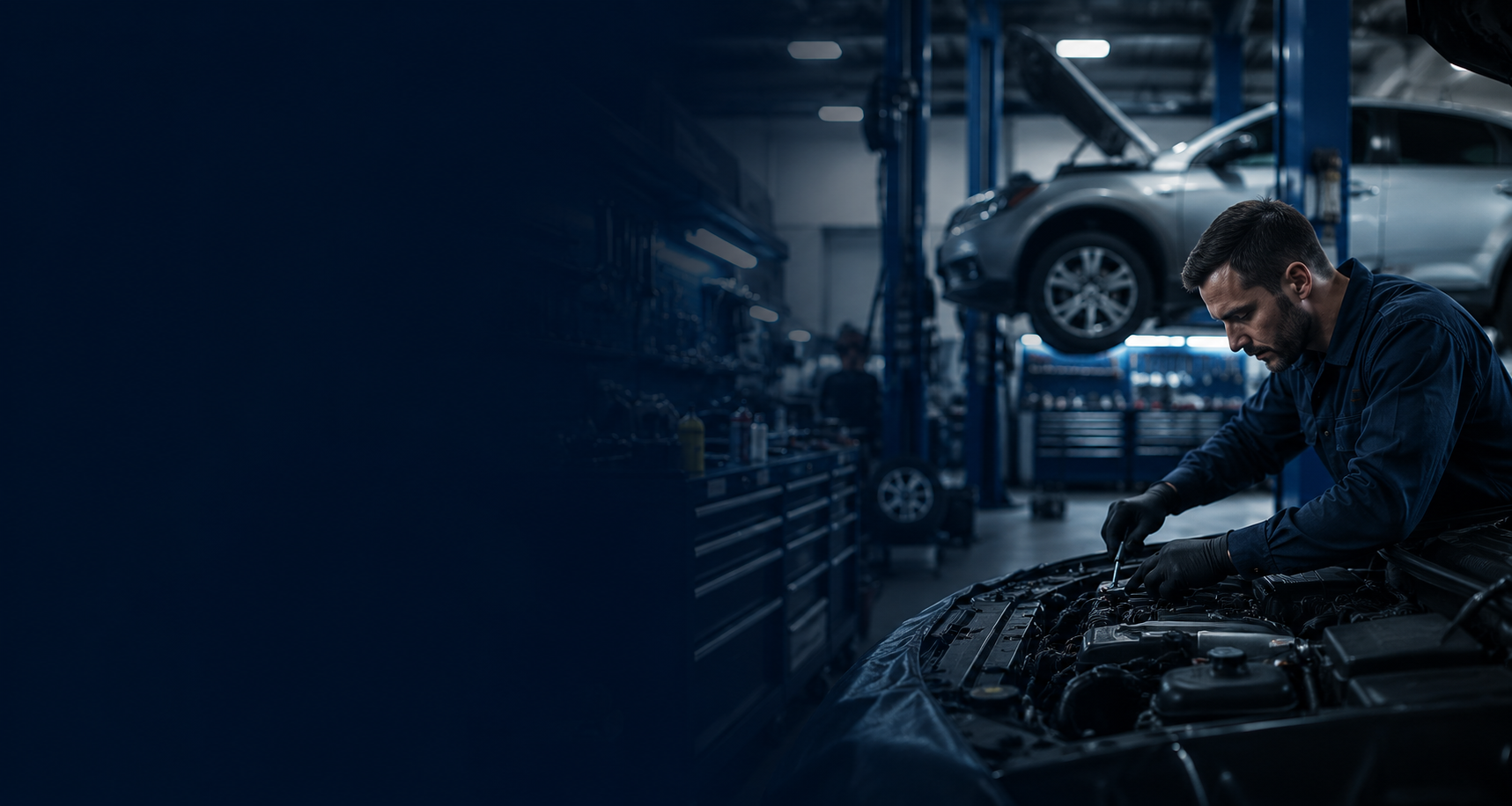 A mechanic working on a car engine in an auto repair garage with cars lifted on hoists in the background.