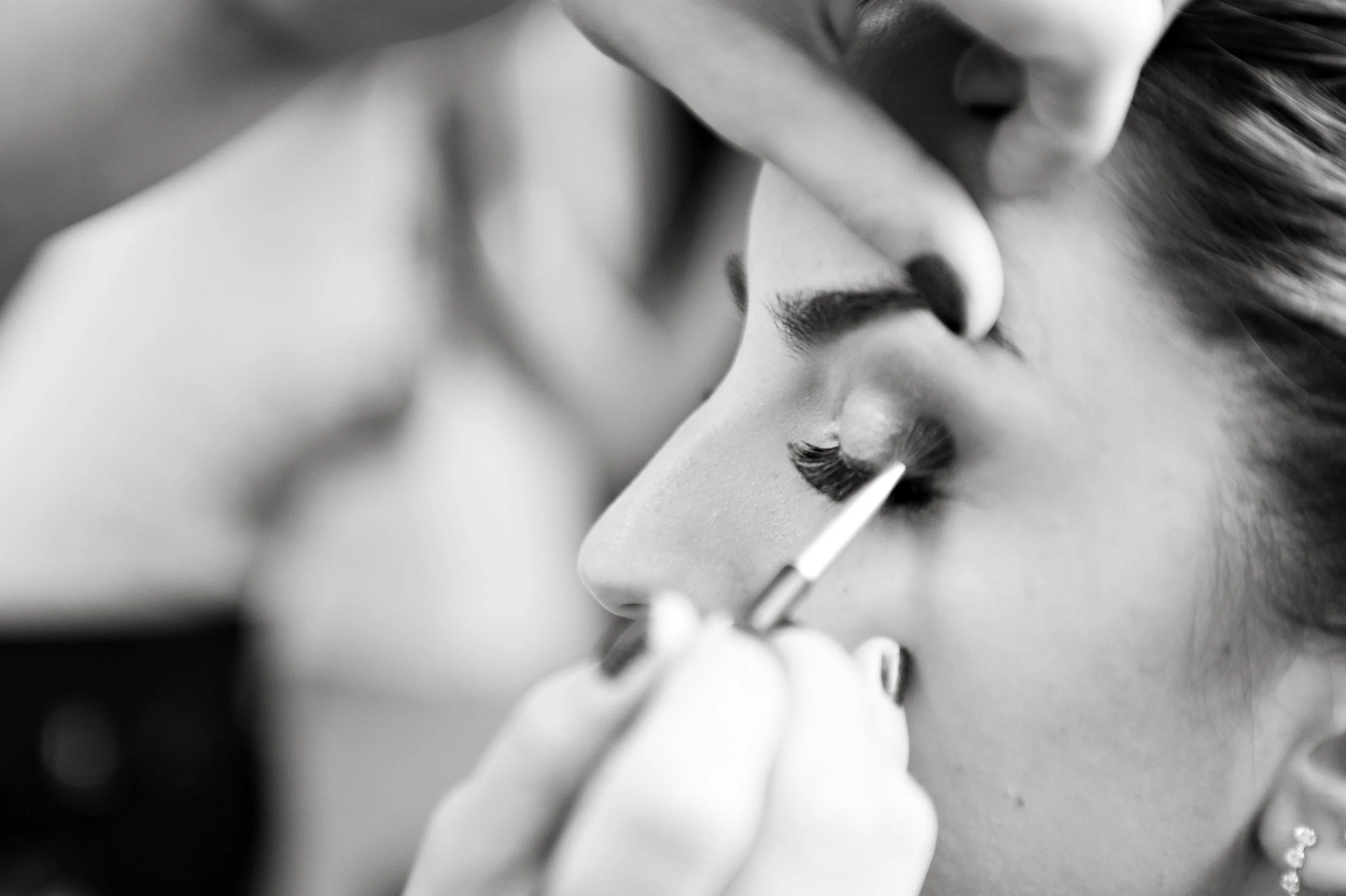 Close-up of a person's face with closed eyes, receiving makeup application with a brush or applicator.