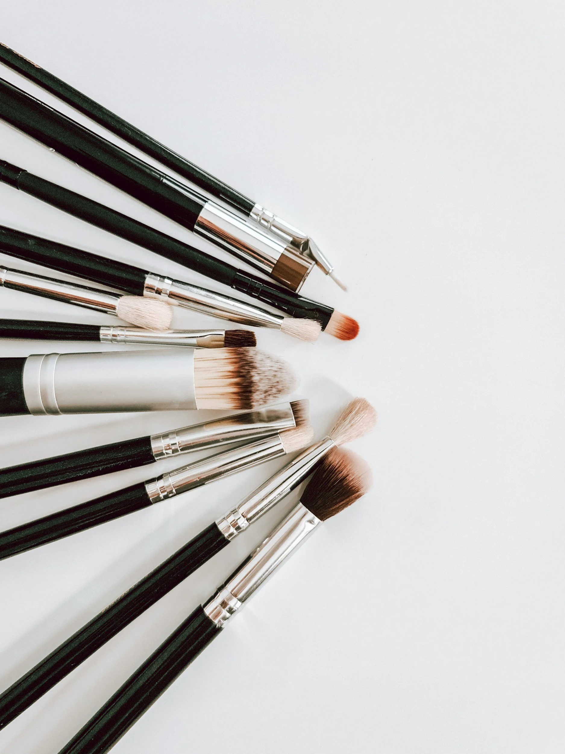 Collection of makeup brushes with black handles and various bristle types, arranged on a white surface.