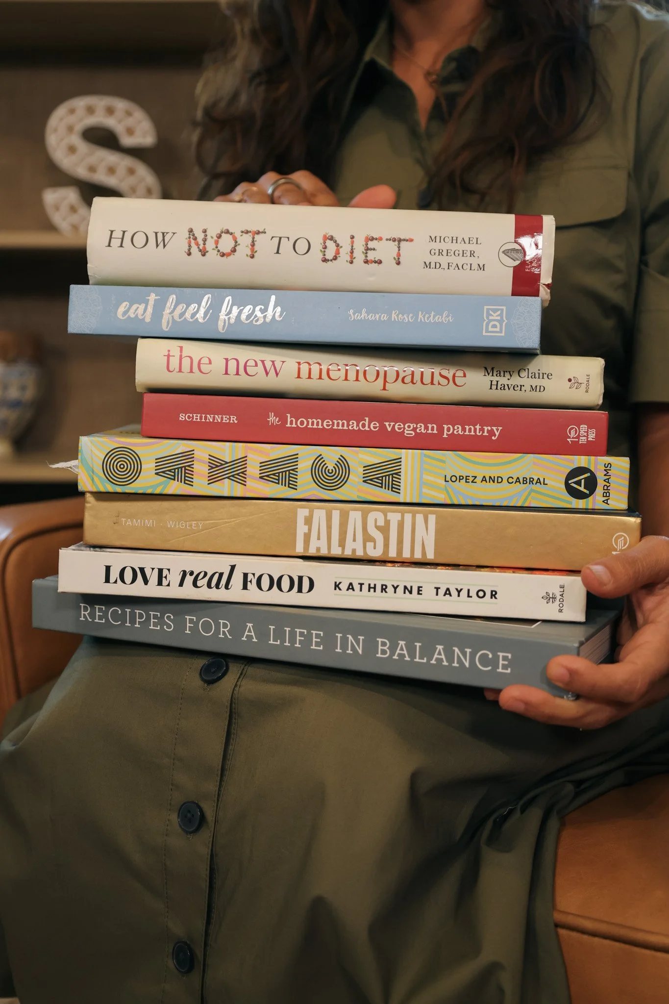 Person holding a stack of books, wearing an olive green jacket.