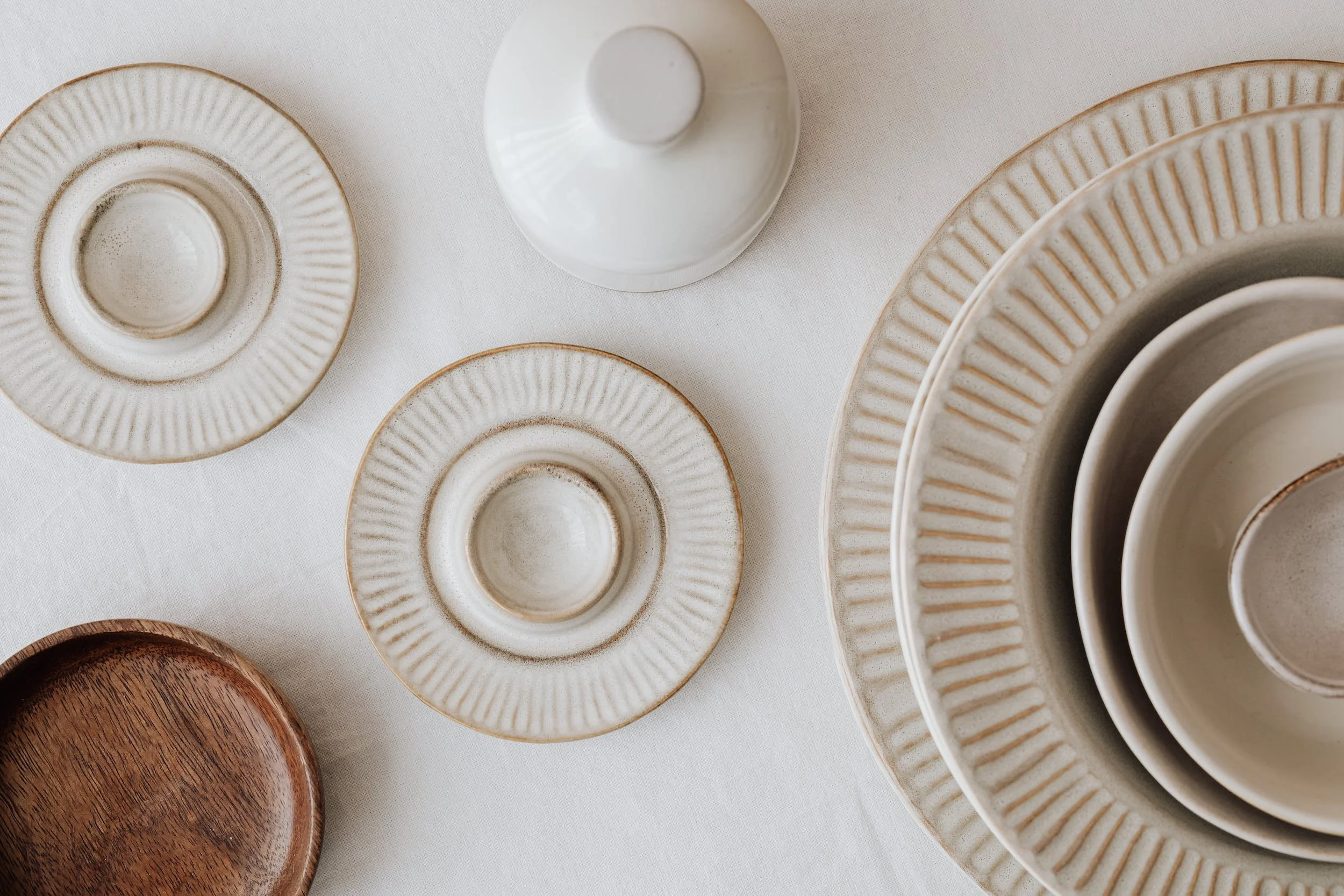 A collection of ceramic plates and bowls, some with ridged or textured rims, arranged on a white surface. The ceramics vary in color, including white, cream, and brown.